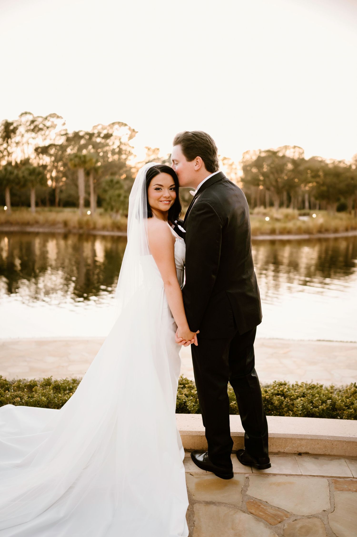 Romantic lakeside wedding portraits with flowing veil at sunset.