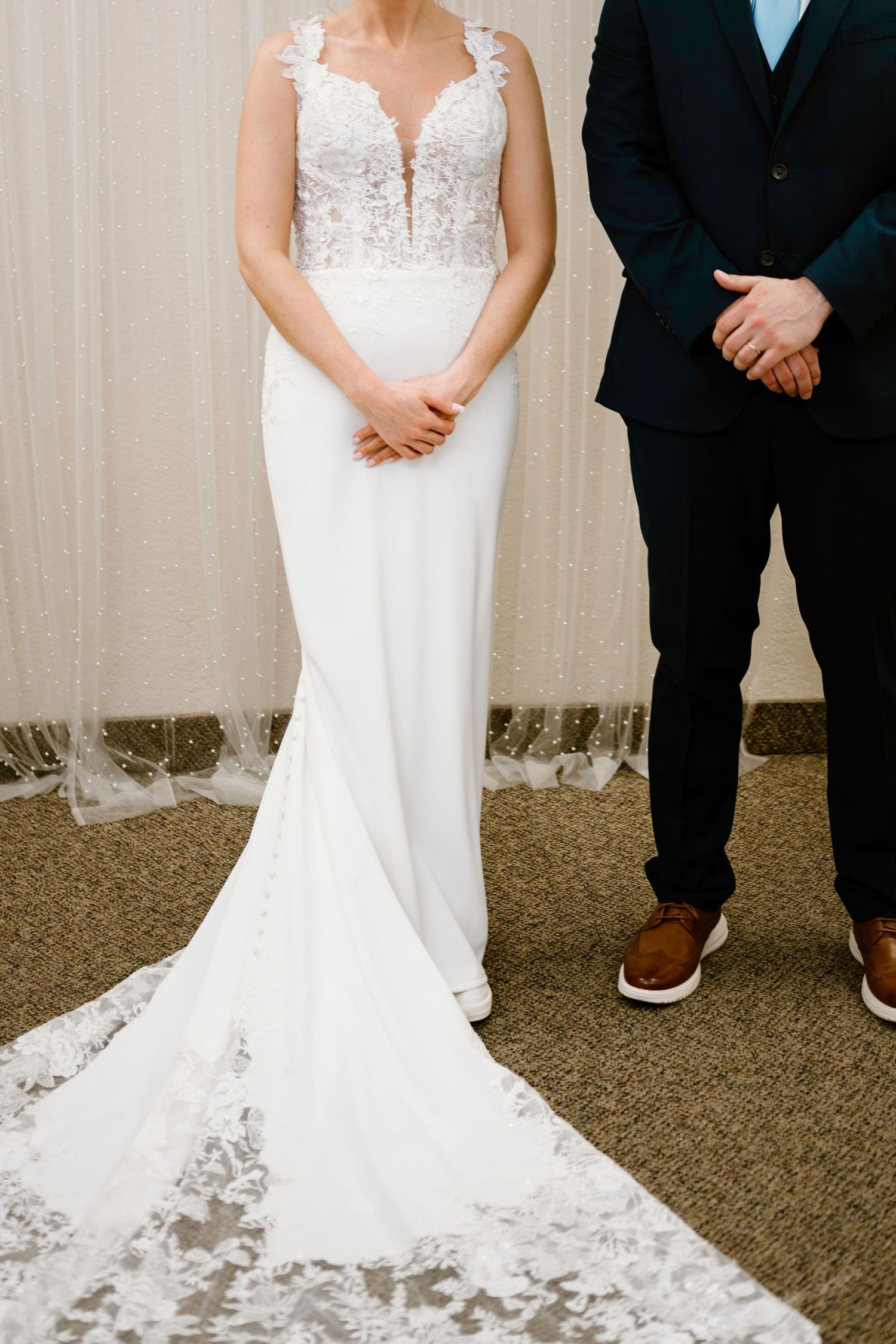 Details of elegant white lace wedding dress with flowing train on carpeted floor.
