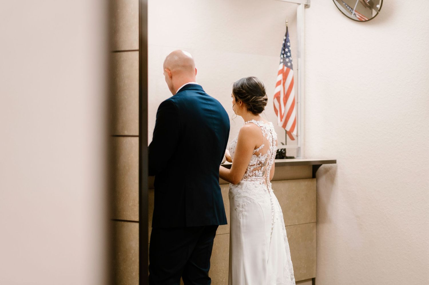 Wedding ceremony taking place in a minimalist indoor venue with American flag visible.