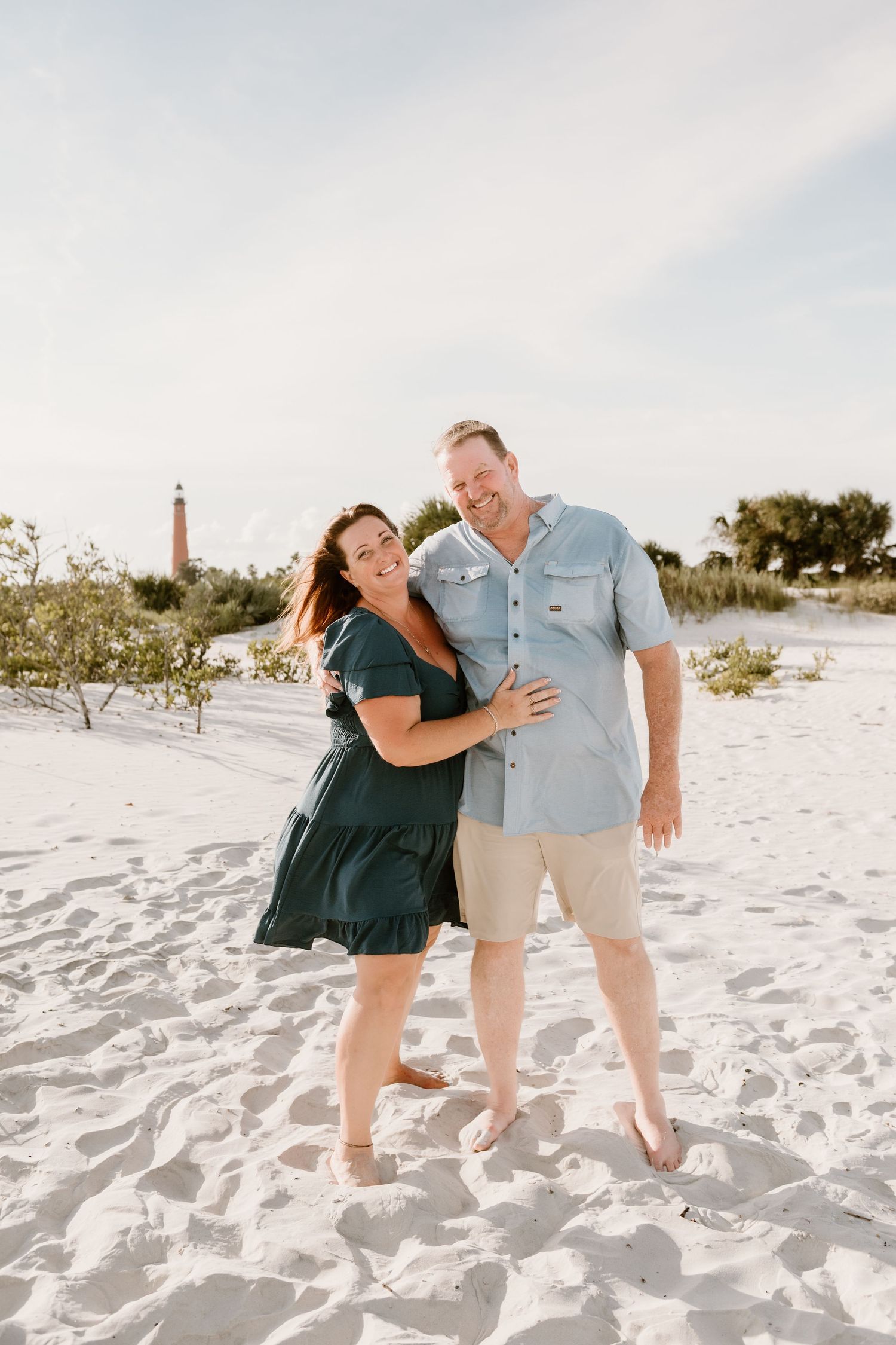 A couple laughs together while posing on pristine white sand during a beach photoshoot.