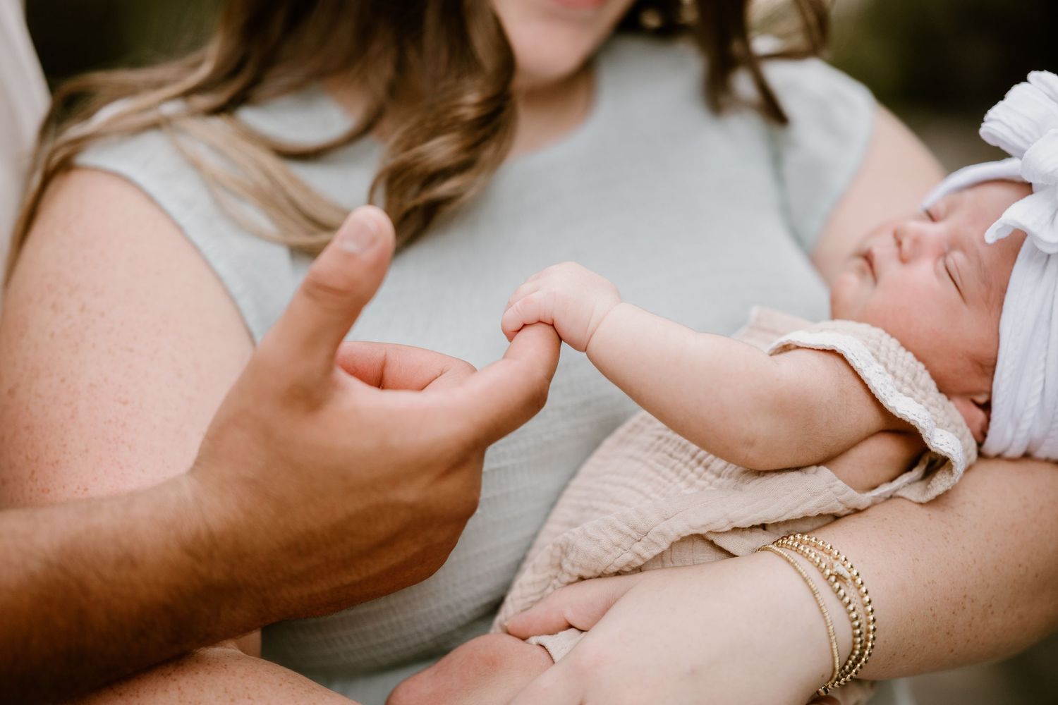 Parents cradle and admire their sleeping newborn baby during an outdoor photo session.