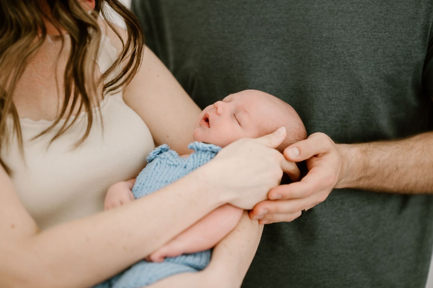 Intimate family moment with a newborn being held tenderly in soft lighting.
