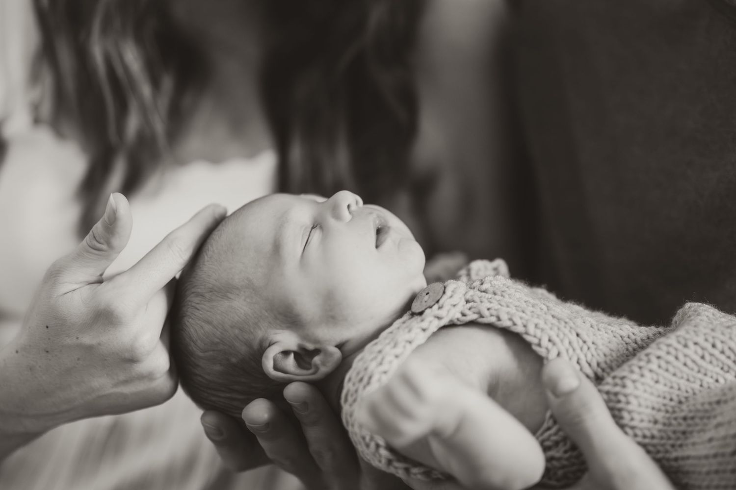Black and white intimate portrait of new parents sharing tender moments with their baby.