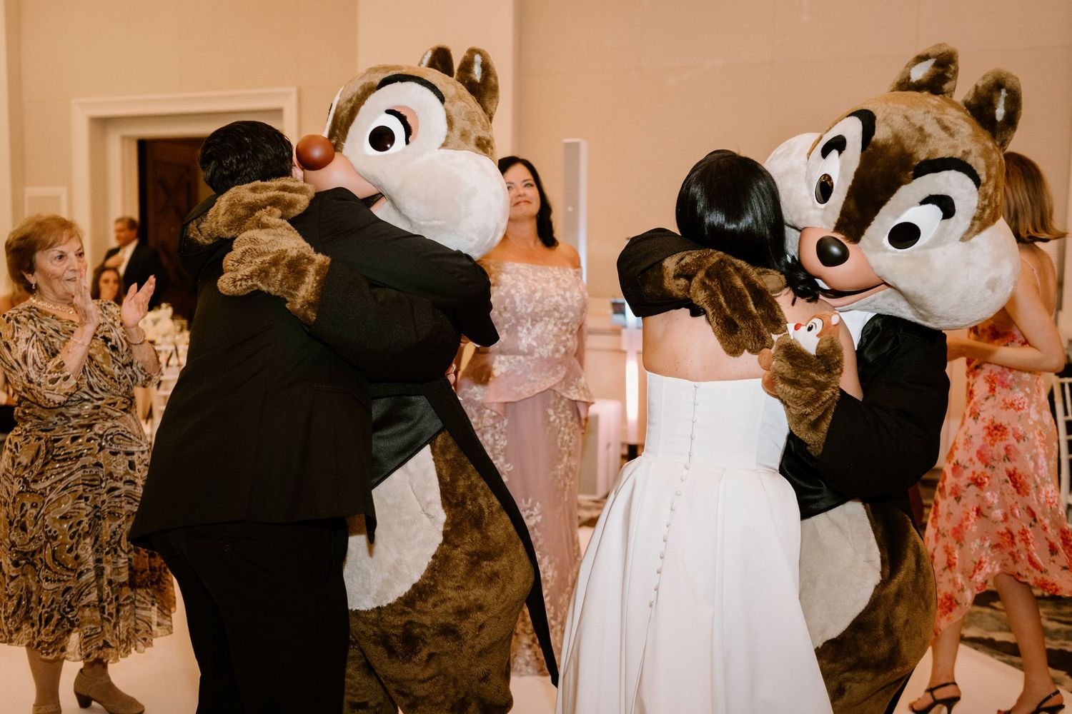 Wedding guests dance with Disney mascot characters during reception celebration.
