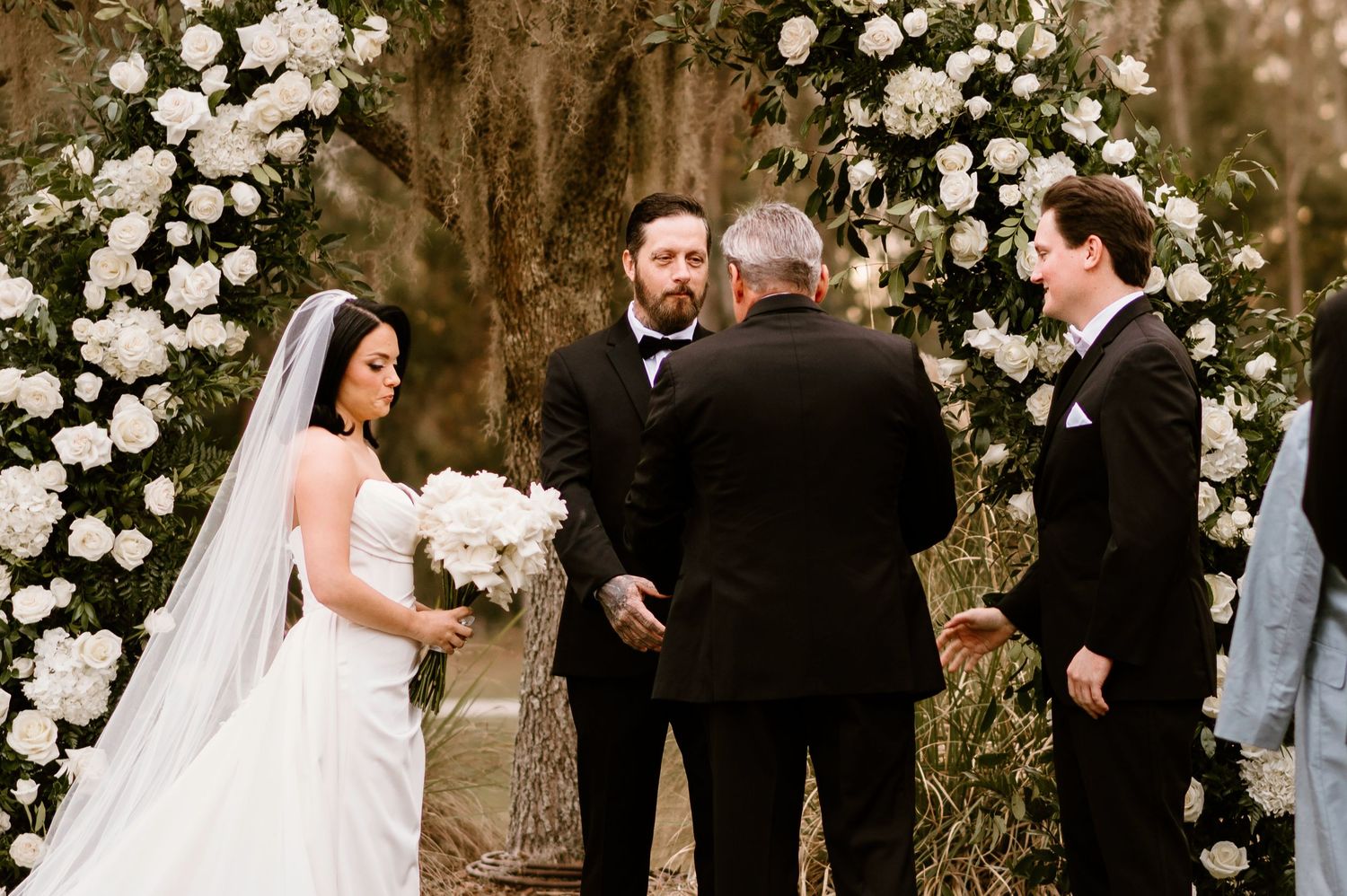 Wedding ceremony under floral arch with white roses and Spanish moss.