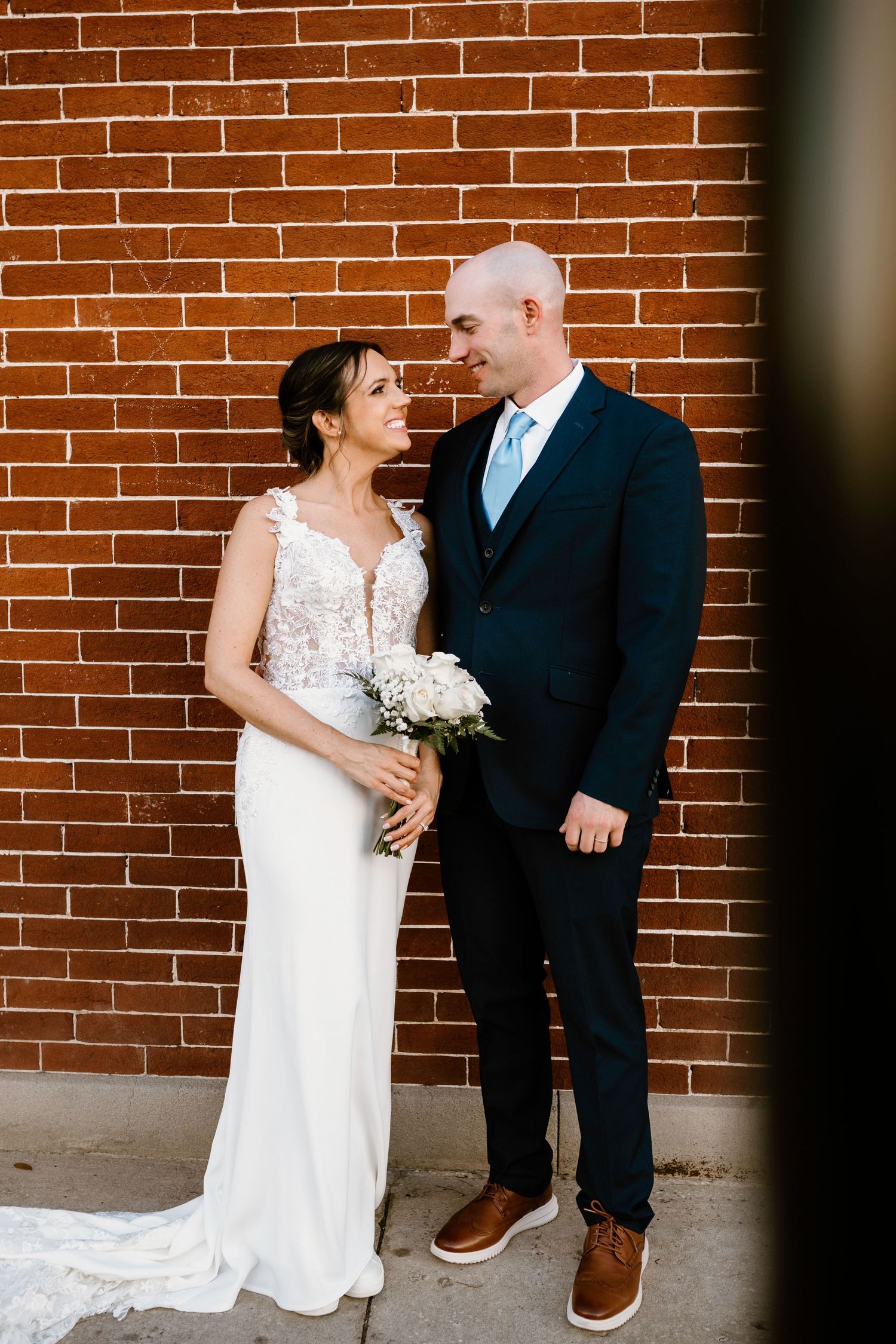 Romantic wedding portraits against rustic brick wall backdrop.