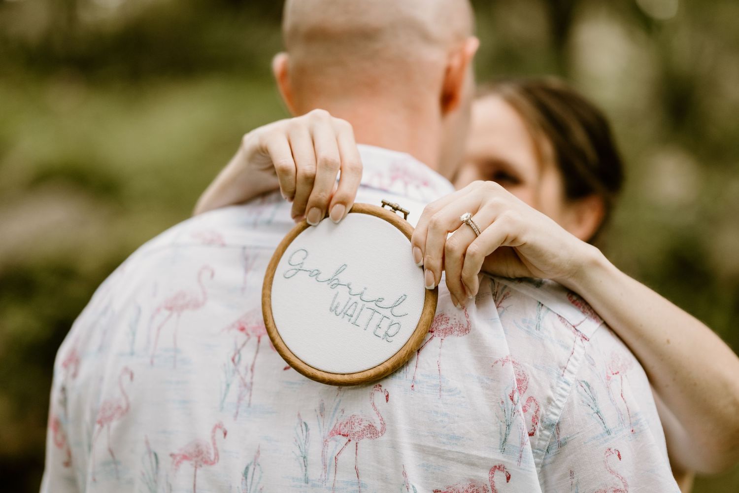 Person holding embroidery hoop against floral shirt during outdoor photo session.