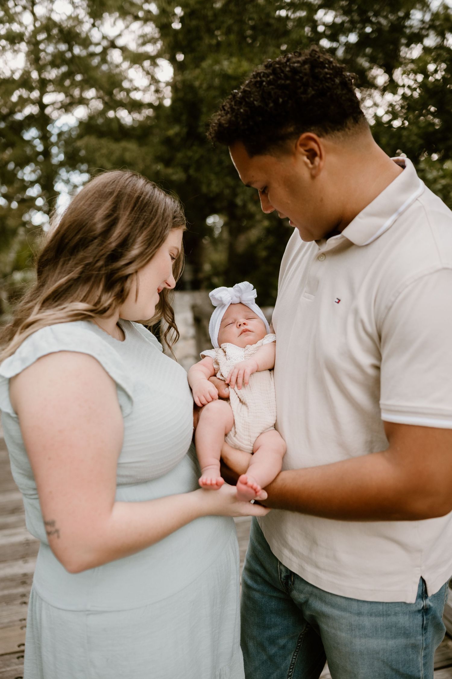 Parents in light colored clothing holding their newborn baby during an outdoor photoshoot.