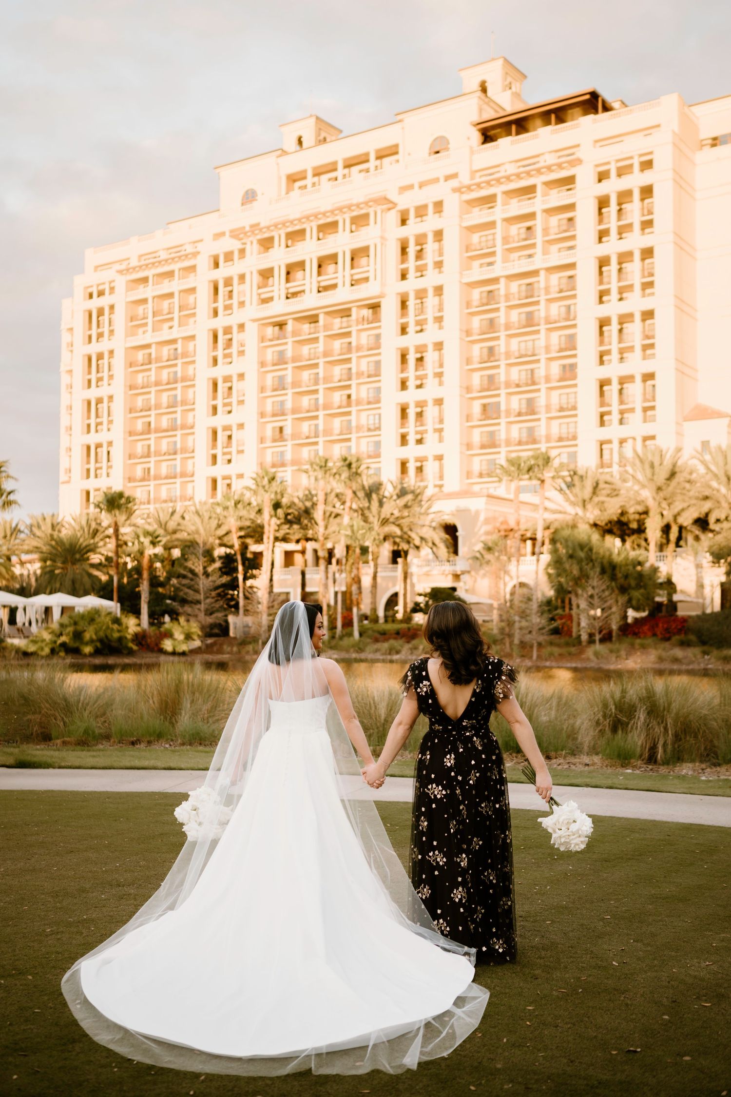 A flowing white wedding dress photographed against a beachfront resort building at sunset.
