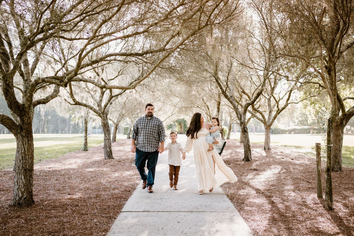 Family walking hand in hand through wooded park during golden hour.