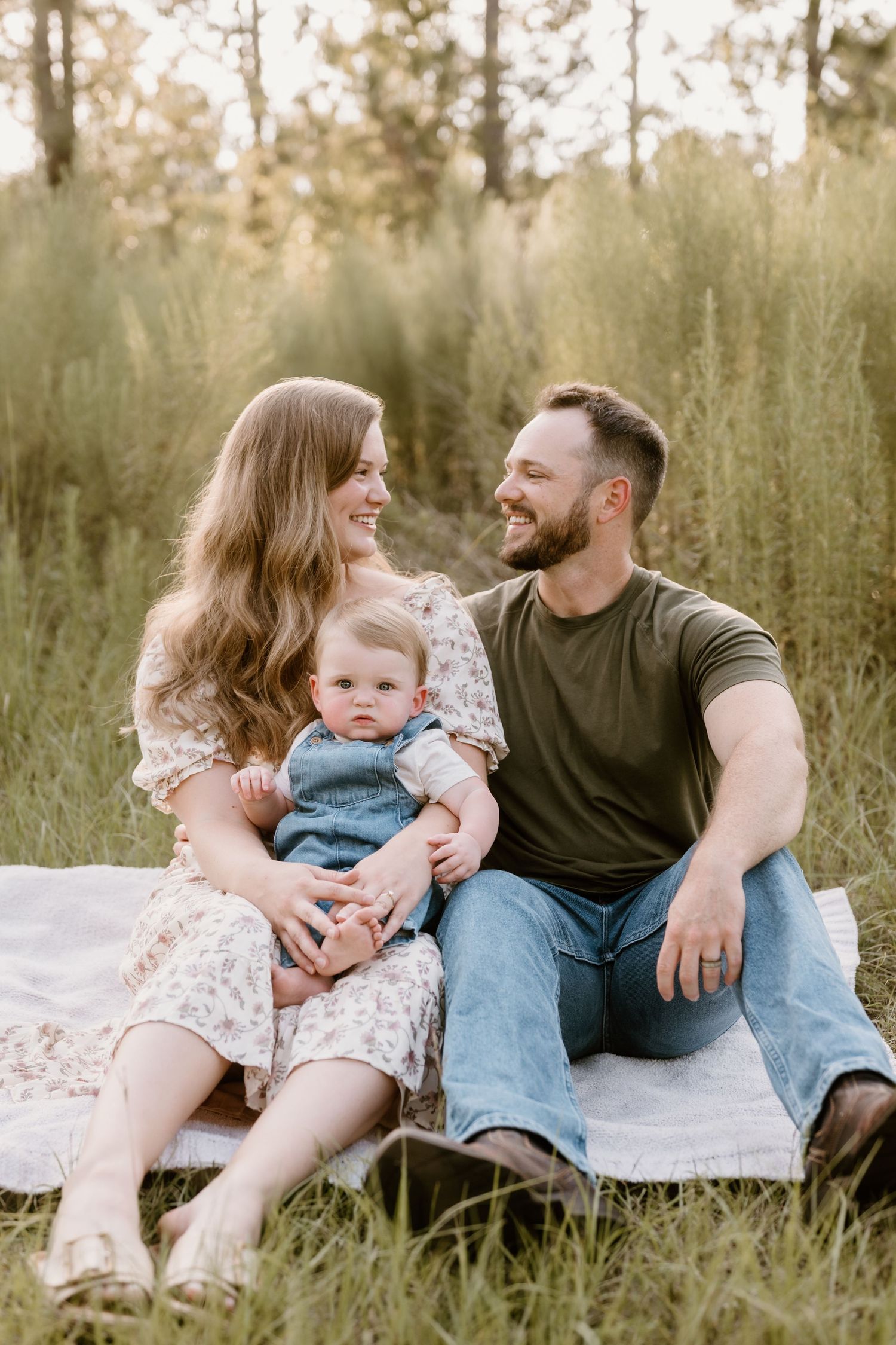 Family relaxing together on a blanket in a field of tall grass during golden hour.