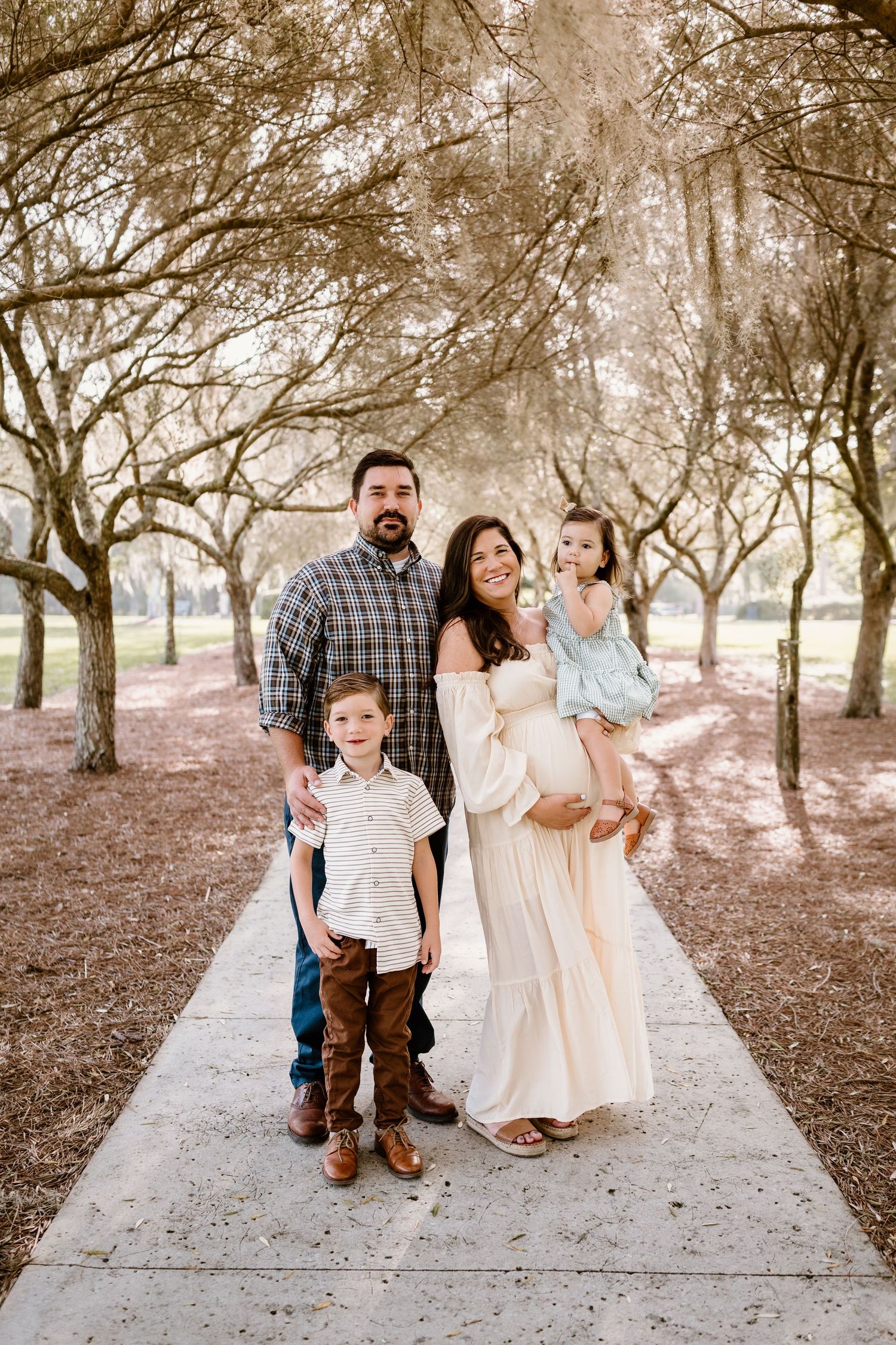 Family poses together on path surrounded by trees during outdoor portrait session.