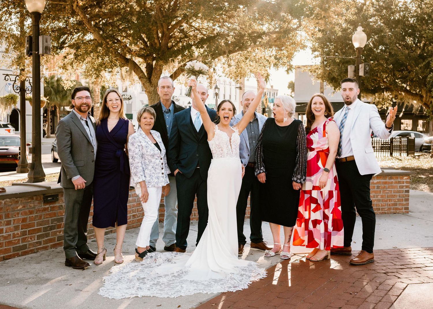 Large wedding party group photos taken outside with brick wall and trees in background.