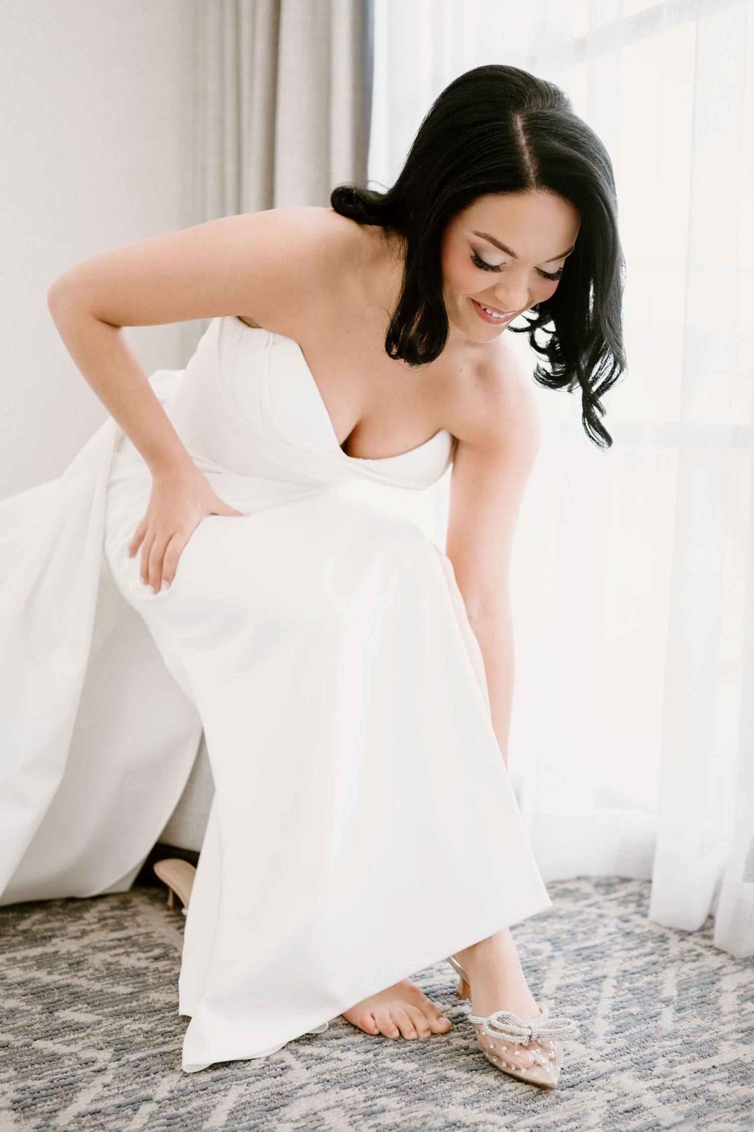 Bride in elegant white dress bends down to fix her footwear.