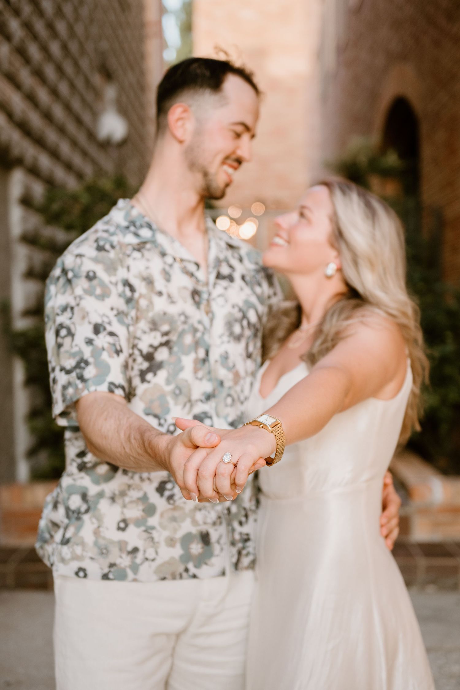 Couple in coordinated white outfits dancing and laughing in a brick-lined corridor.