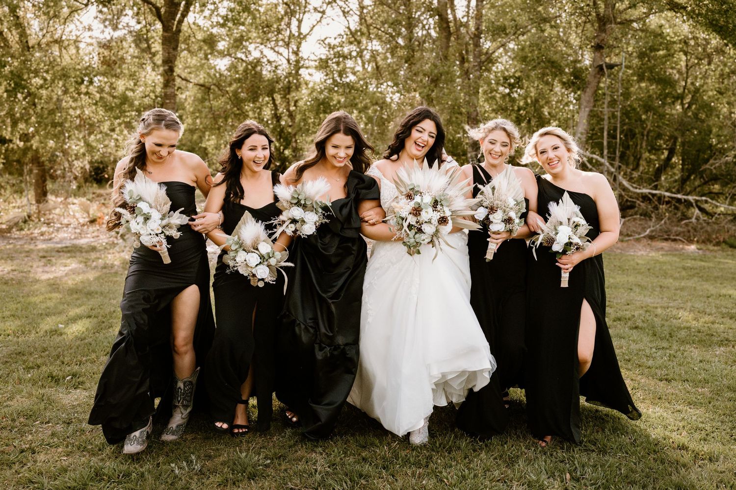 Bridal party sitting casually on grass in black dresses with white bouquets.