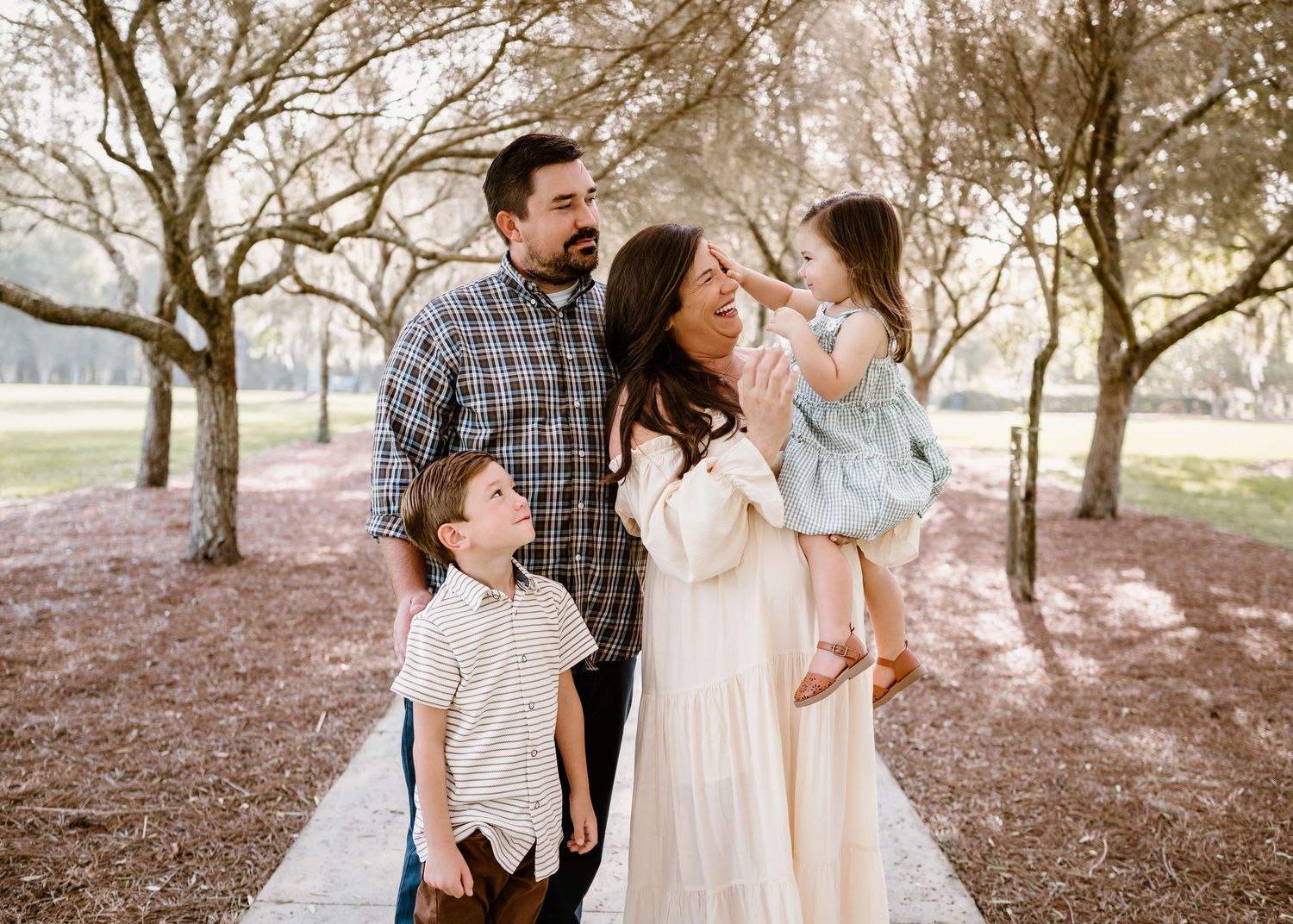 Family portrait under blooming trees with soft pink tones and natural lighting.