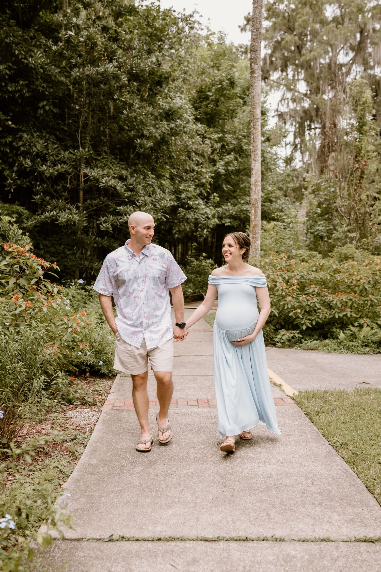Couple walking on garden path during maternity photoshoot.