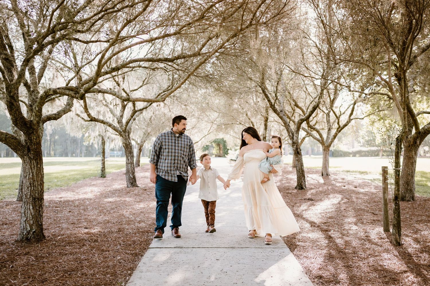 Family walking together through a sunlit tree-lined path during a photo session.