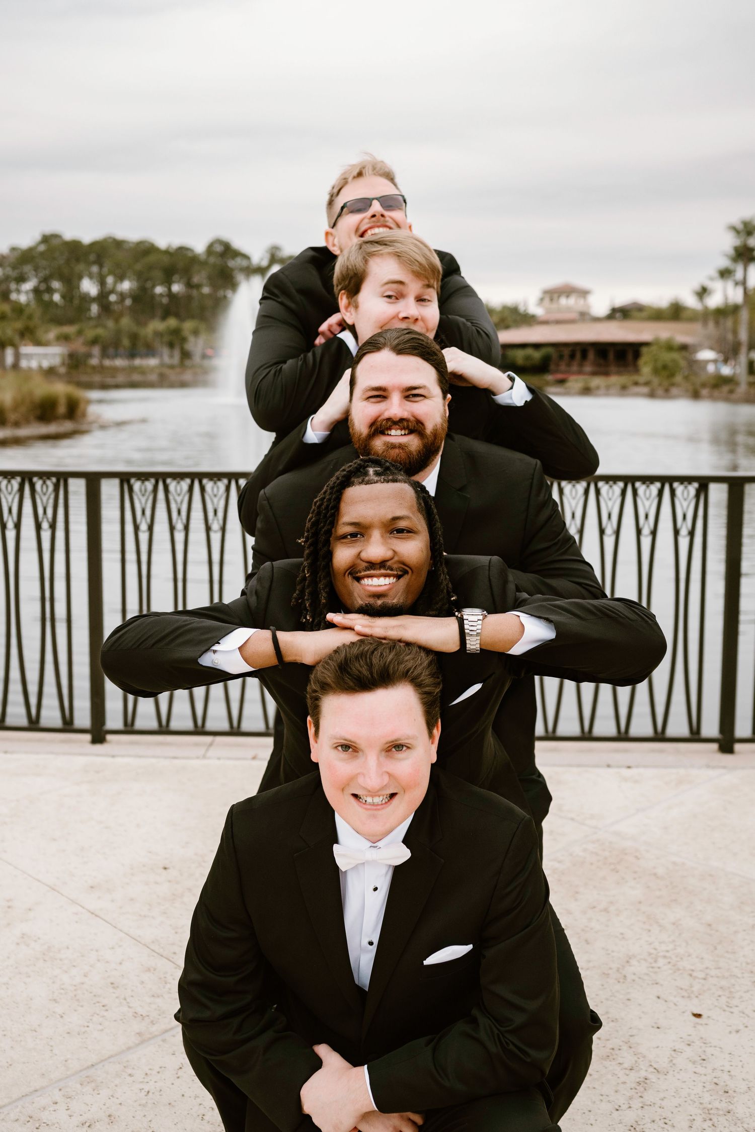 Groomsmen stacked in a fun pyramid pose on an outdoor terrace.