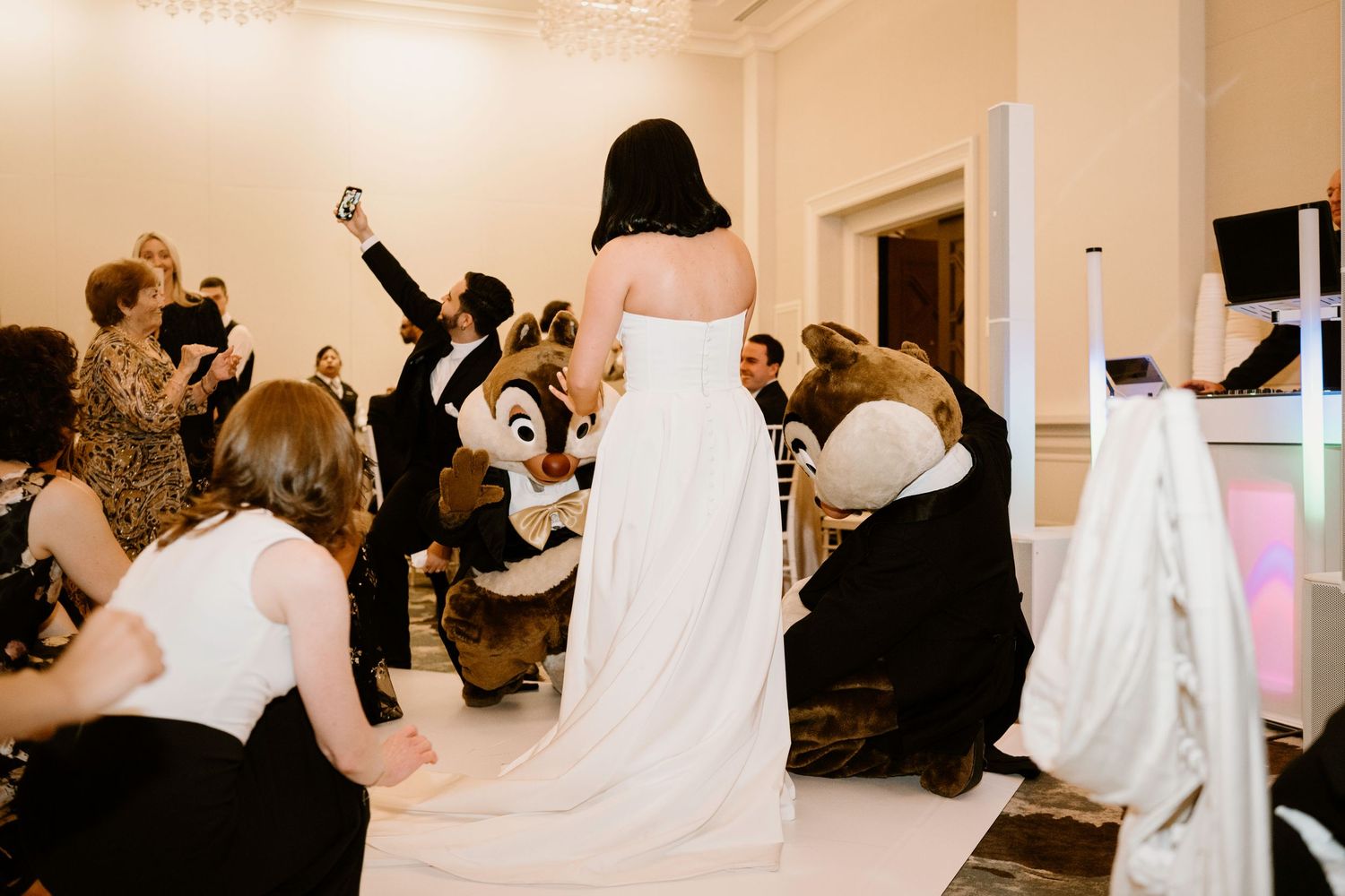 Disney character Chip or Dale mascot dances with wedding guests in an elegant reception hall.