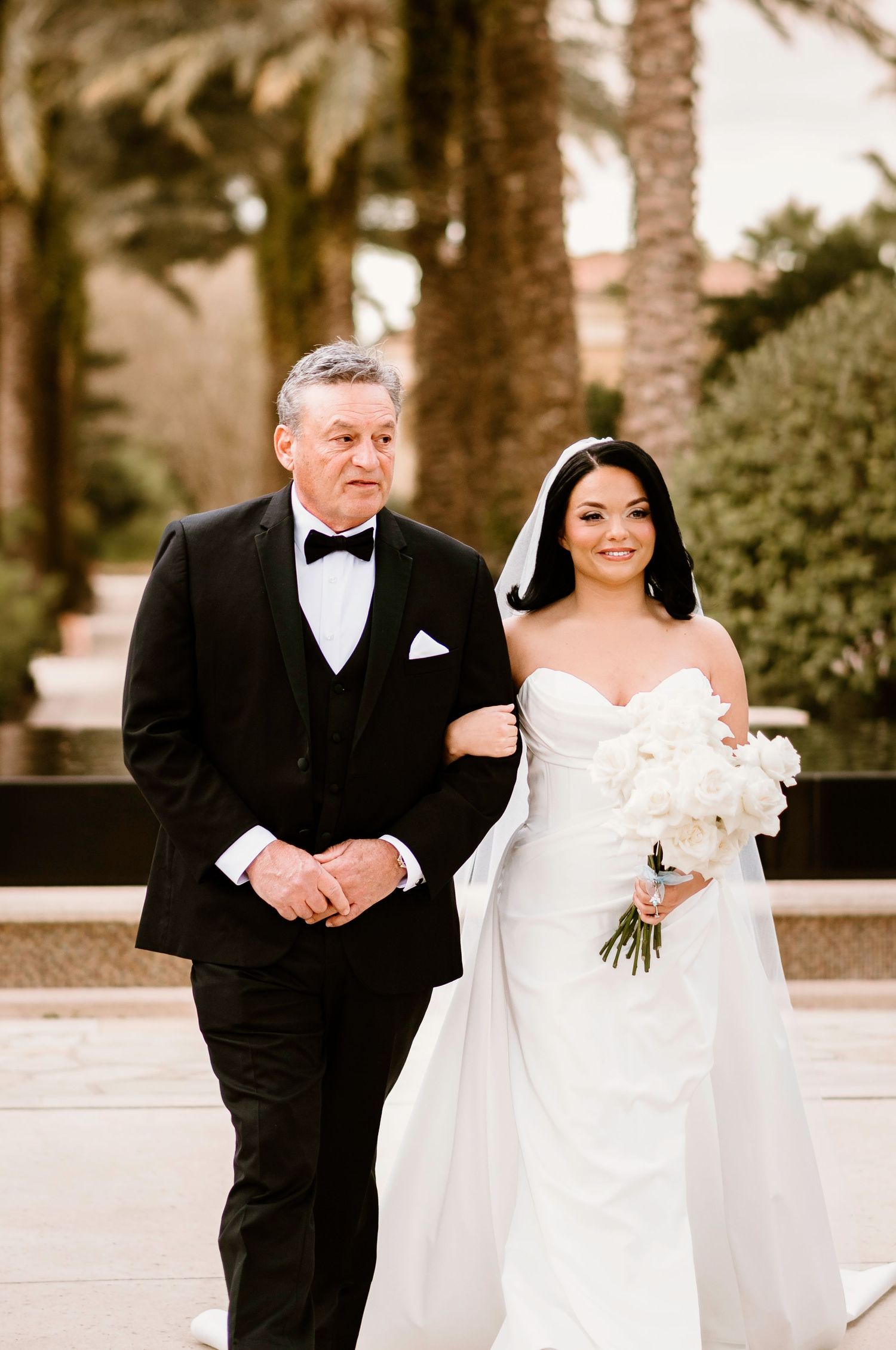 A wedding couple poses outdoors among palm trees at an elegant venue.