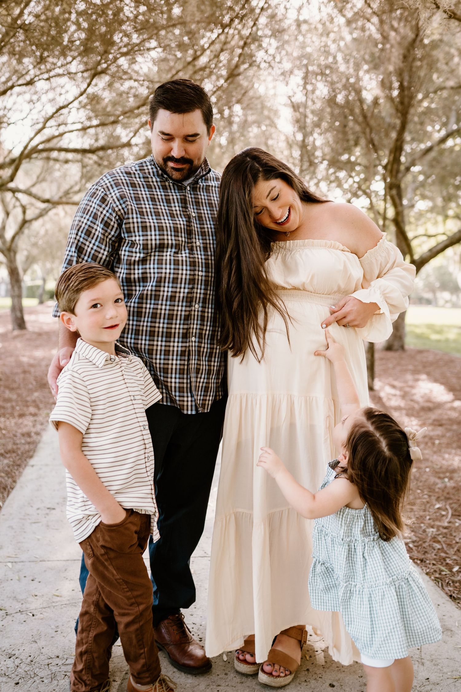 A family stands together on a sunlit path surrounded by trees.