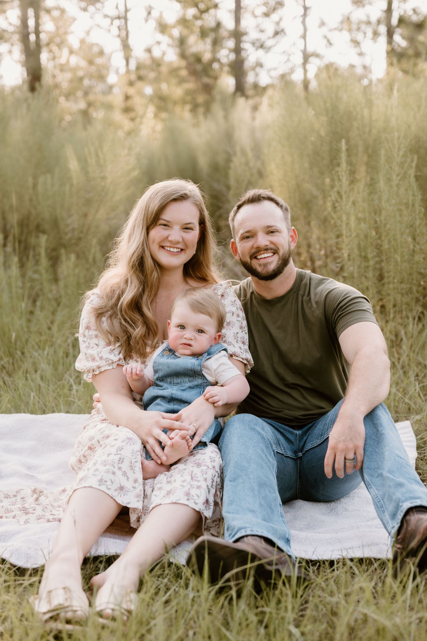 Family relaxing on blanket in grassy field during outdoor photo session.