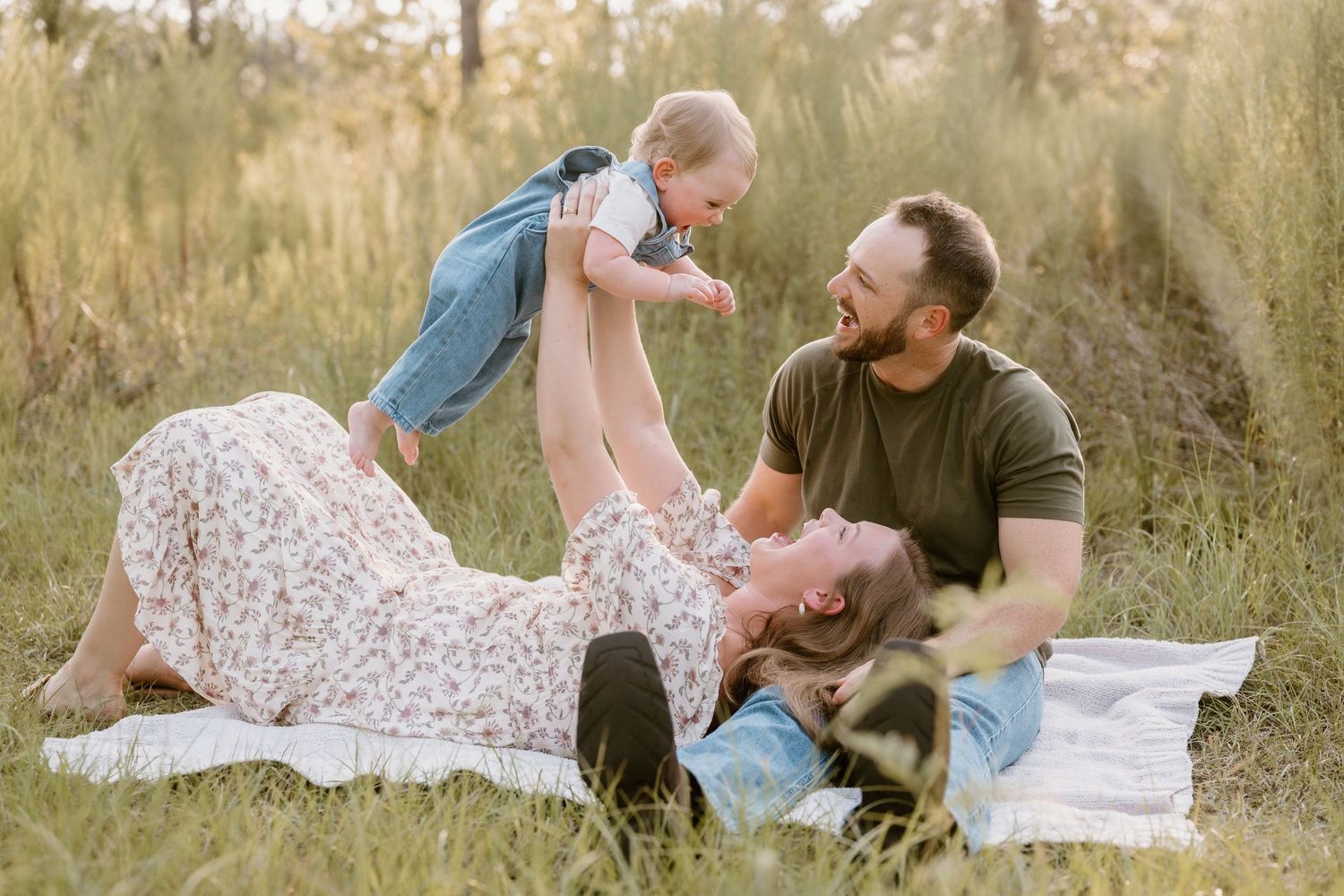 A loving family plays together on a blanket in a sunlit field with tall grass.