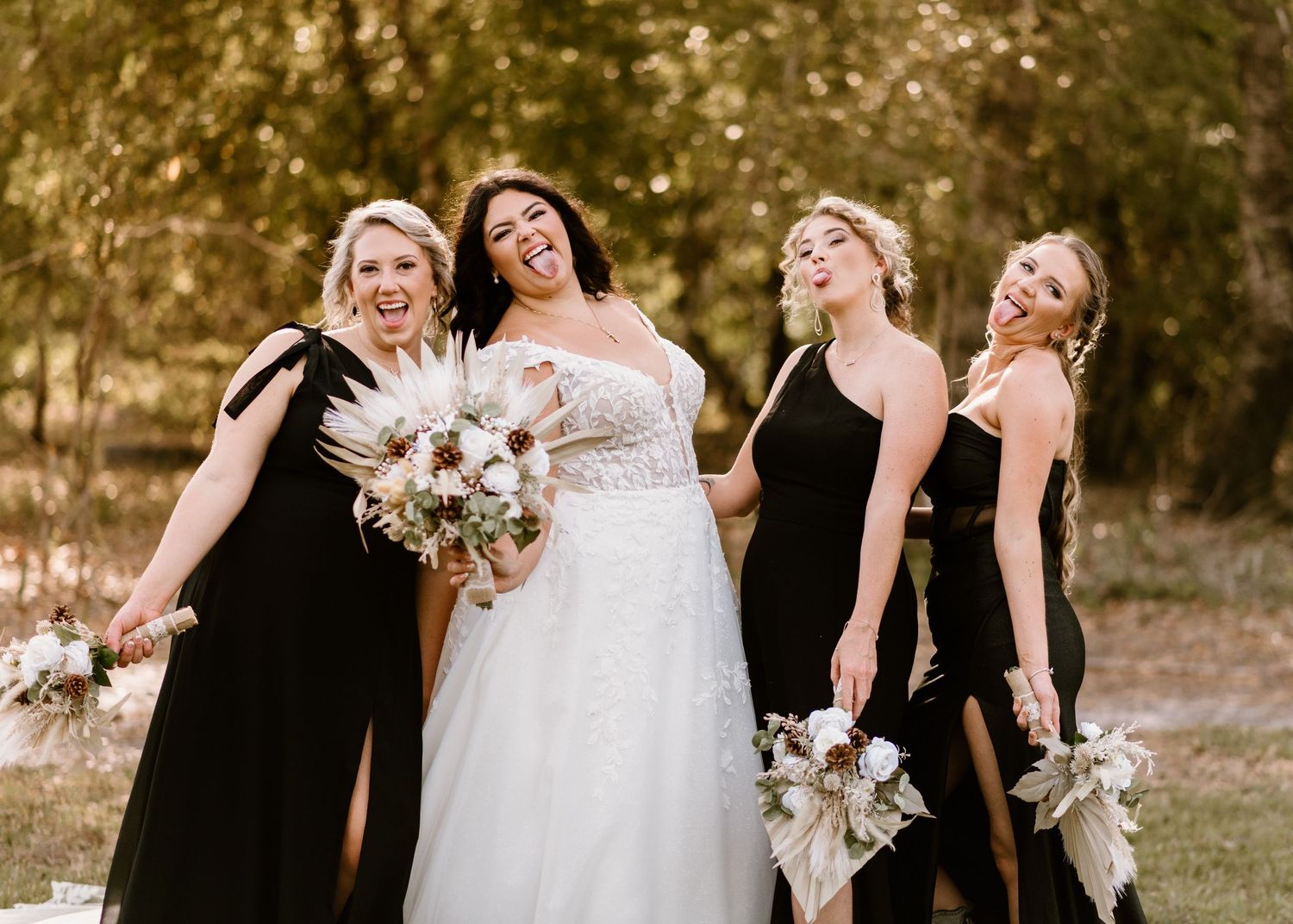 Wedding party in black dresses and white gown pose together outdoors.