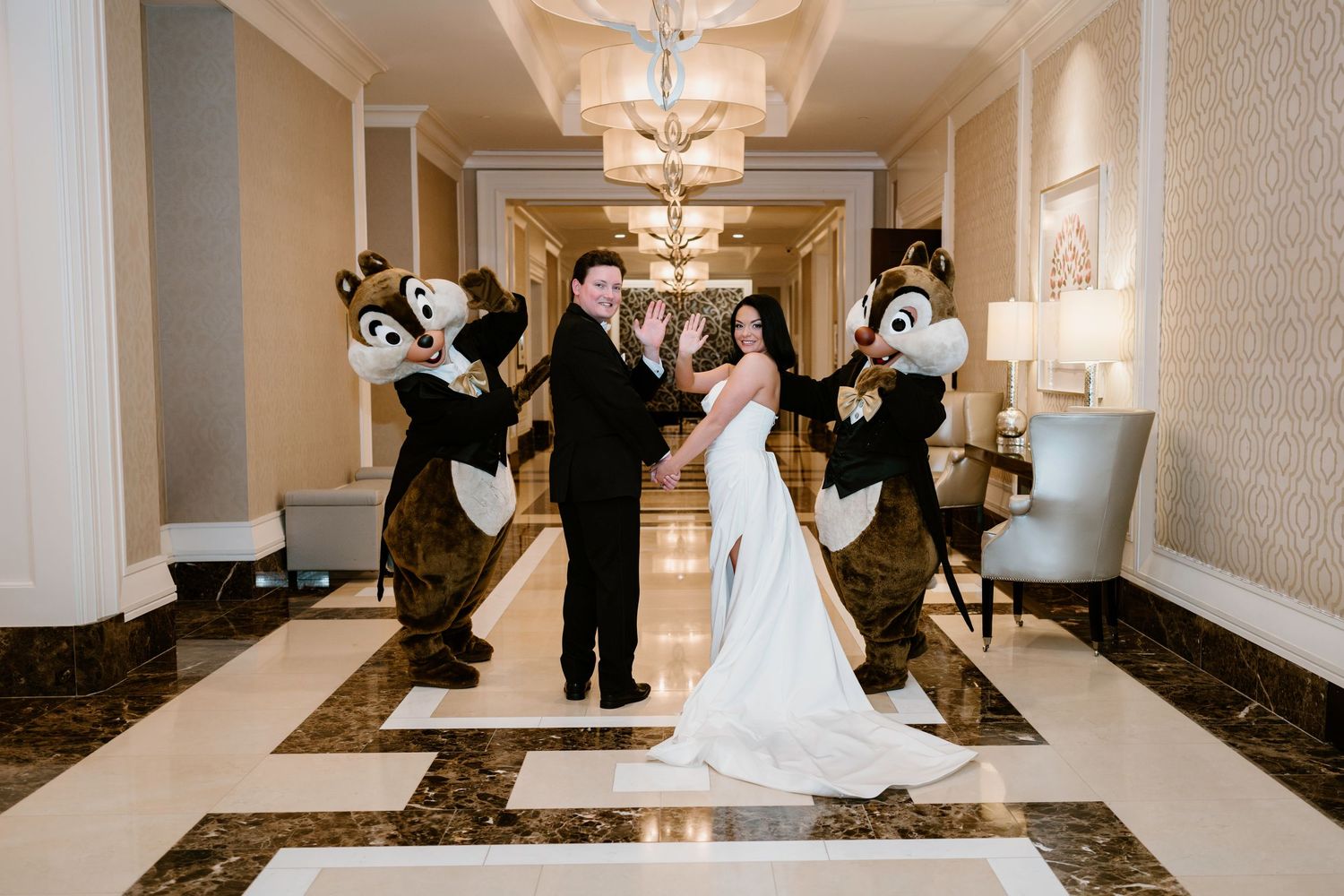A wedding party poses with Chip and Dale mascots in an elegant hotel hallway.