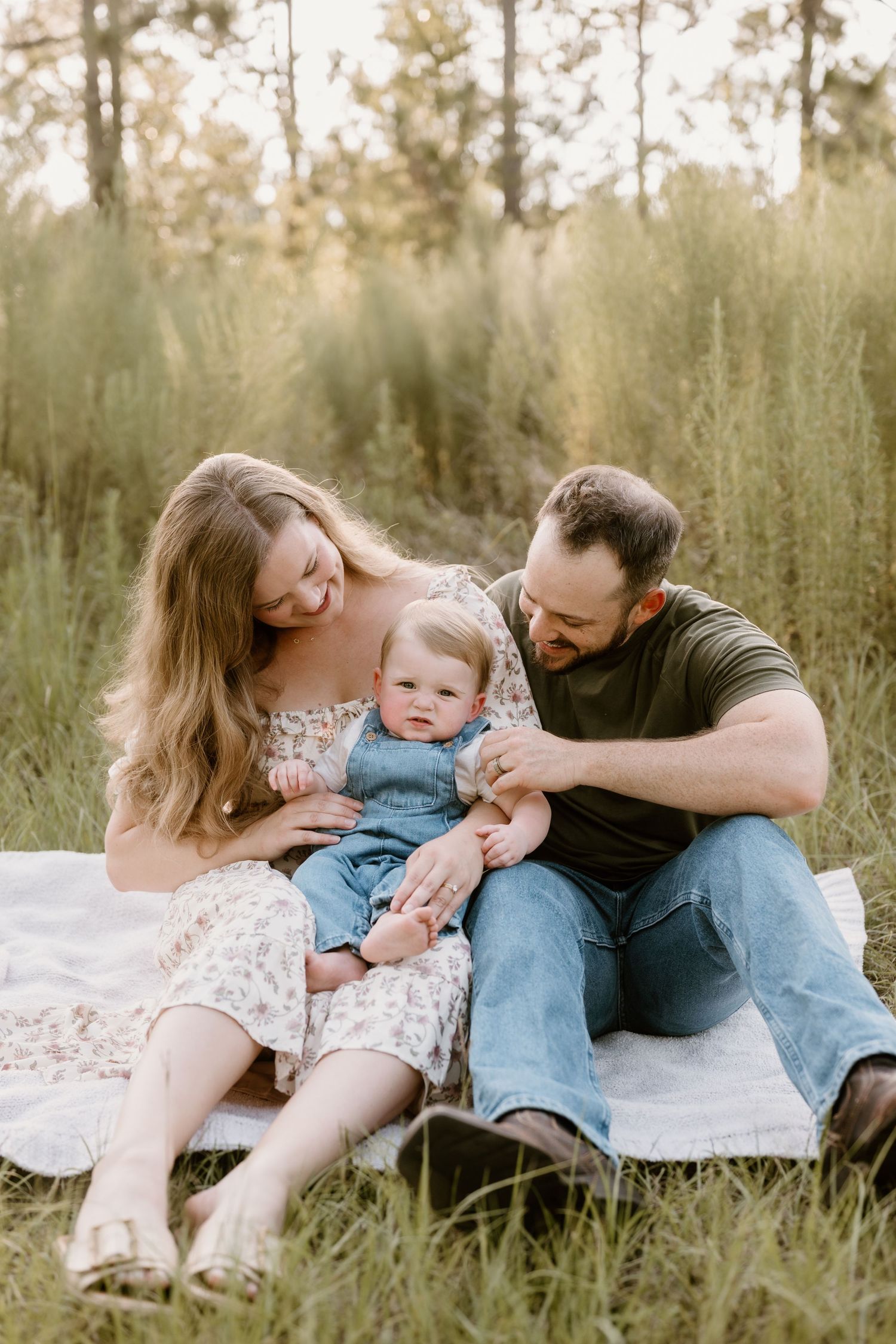 Family sharing tender moments while sitting on blanket in grassy field during sunset.