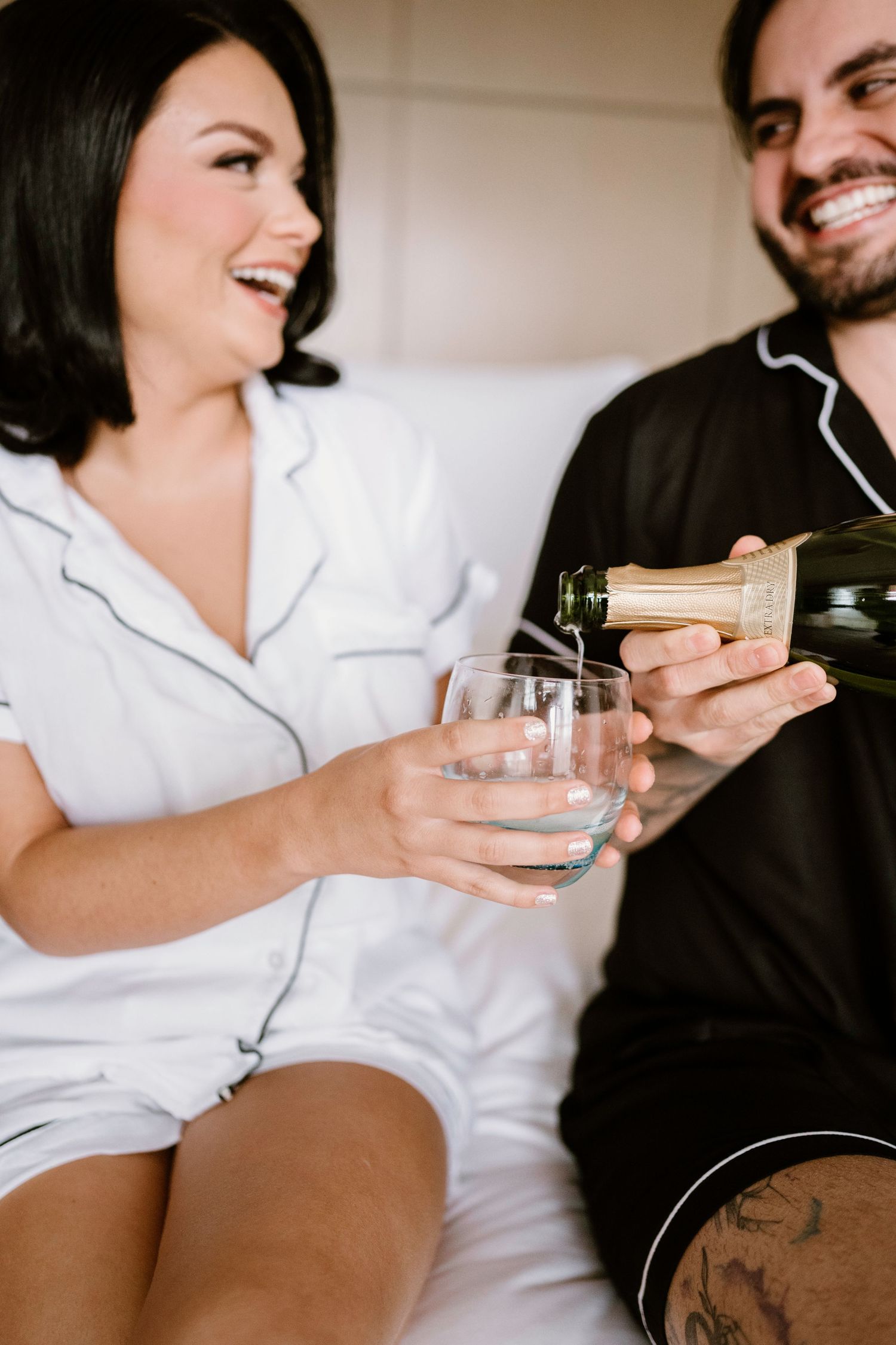 Two people share drinks and laughter while sitting together in casual attire.