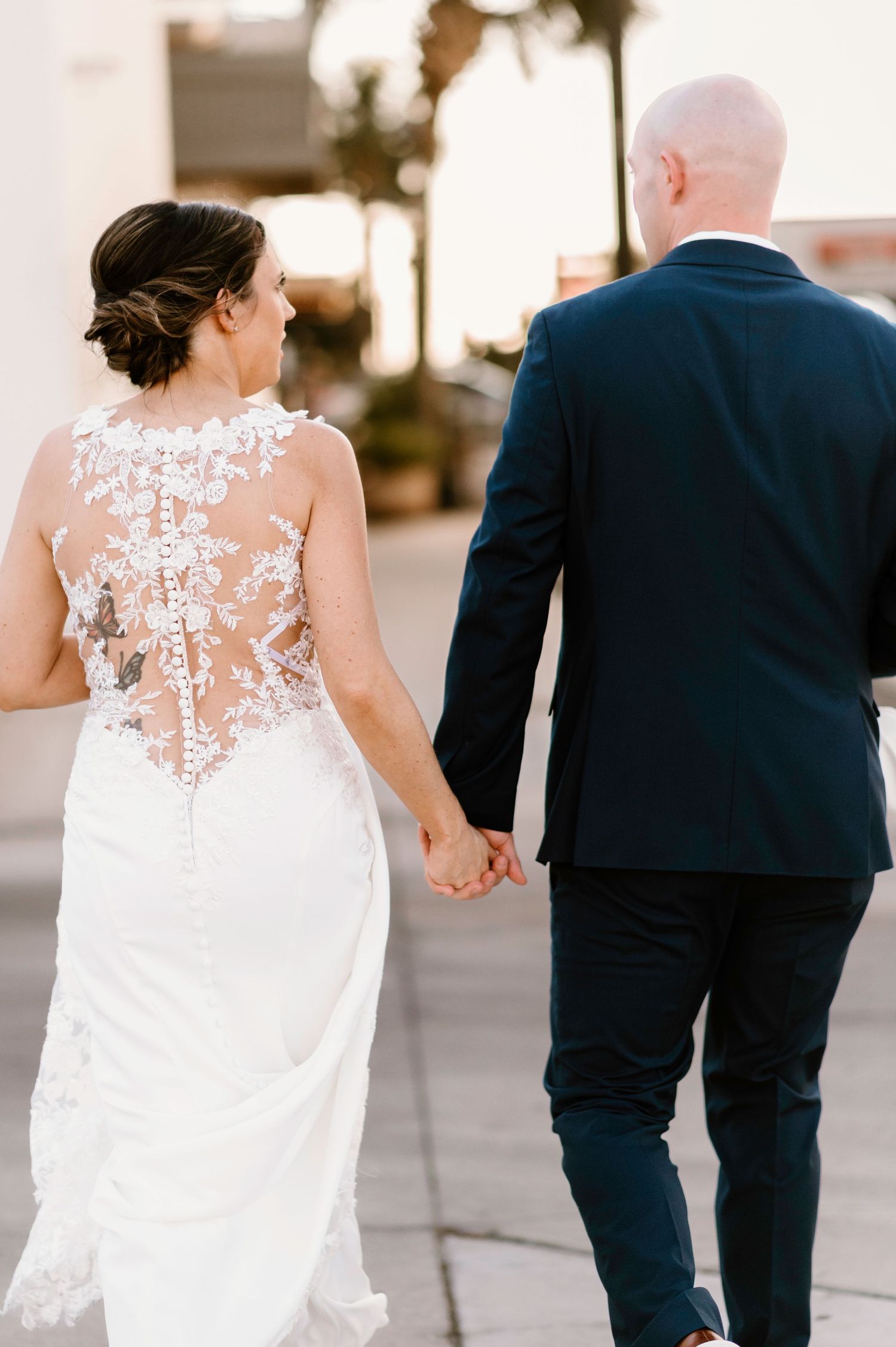 Back view of wedding couple walking together showing intricate lace details on bride's dress.