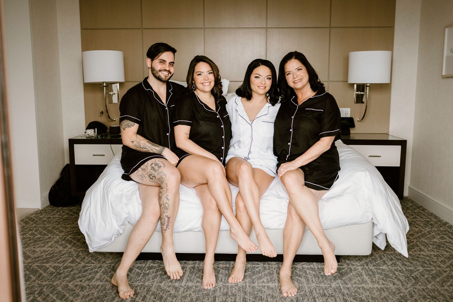 Friends sitting in a row on a hotel bed showing their legs in a fun group photo.
