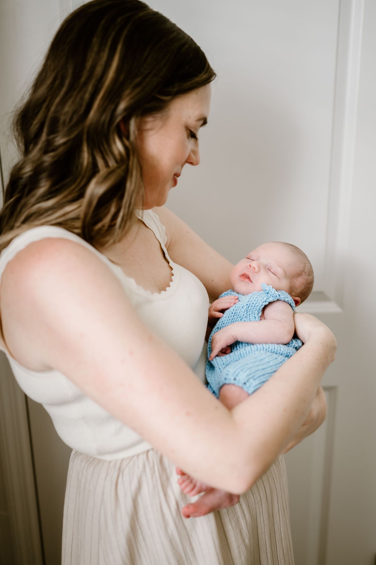 A tender moment as a newborn in a light blue outfit is cradled gently against a white dress.