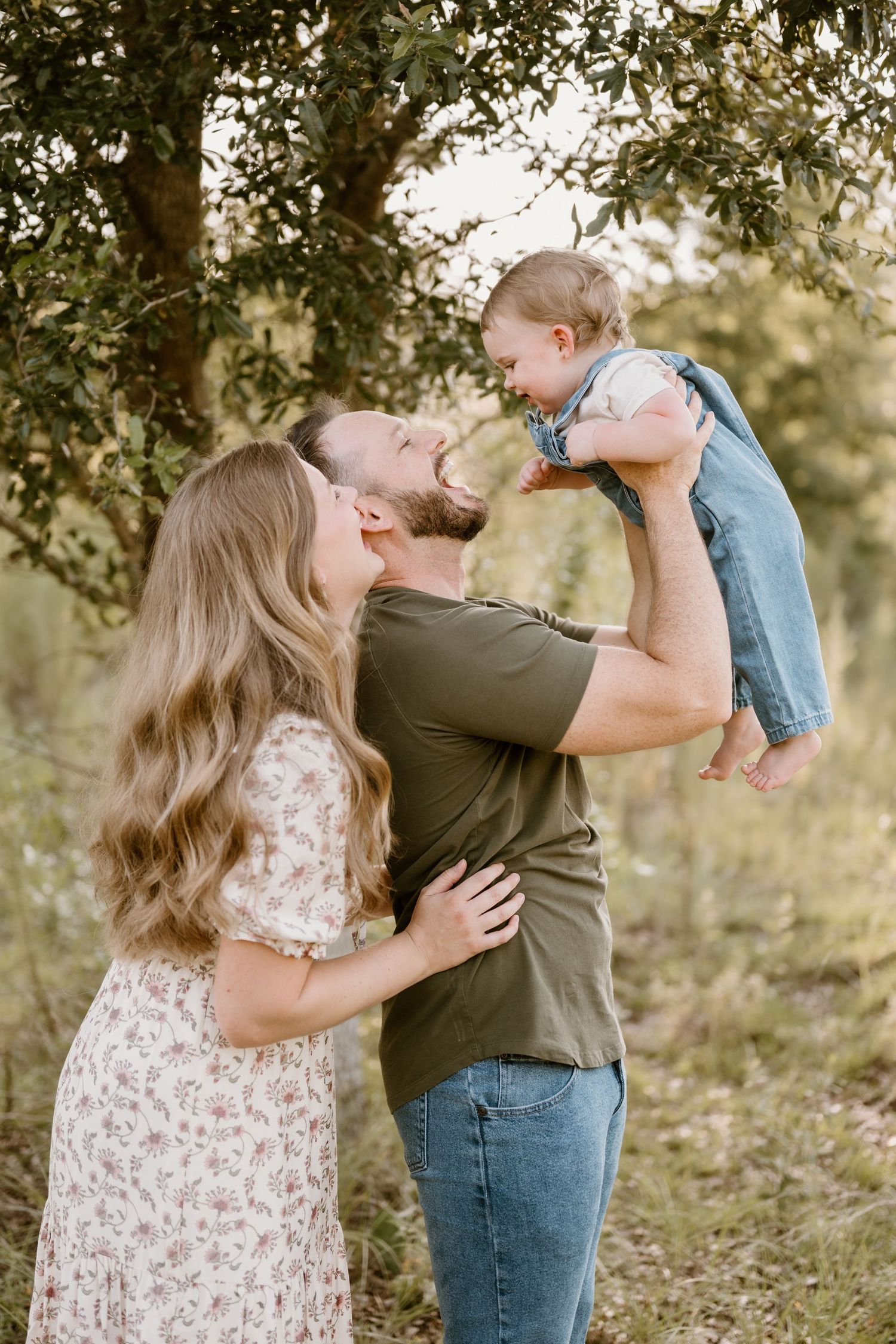 A family shares joyful moments together in a sun-dappled outdoor setting with trees in the background.