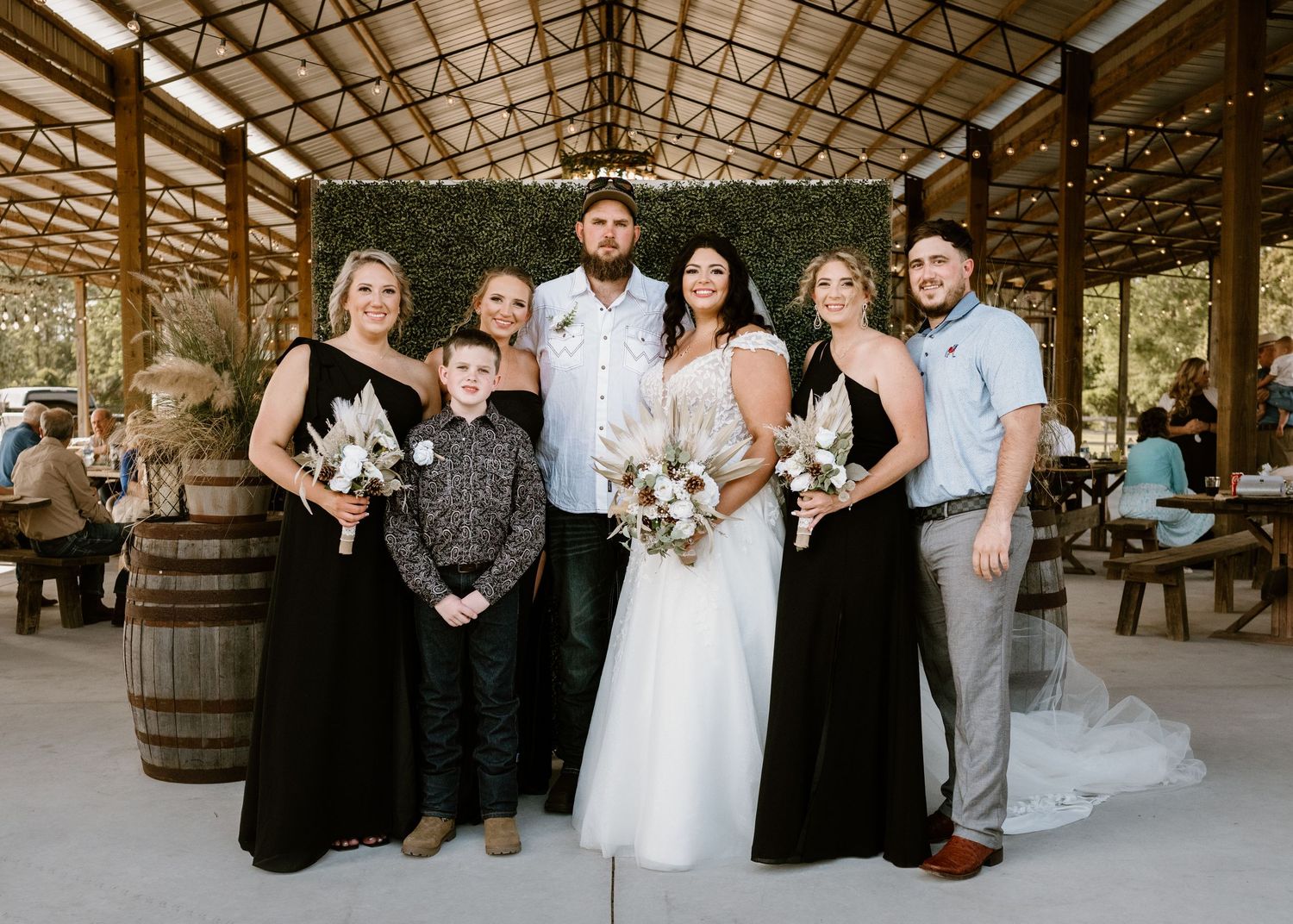 Wedding party poses together in rustic covered venue with barrels and wooden beams.