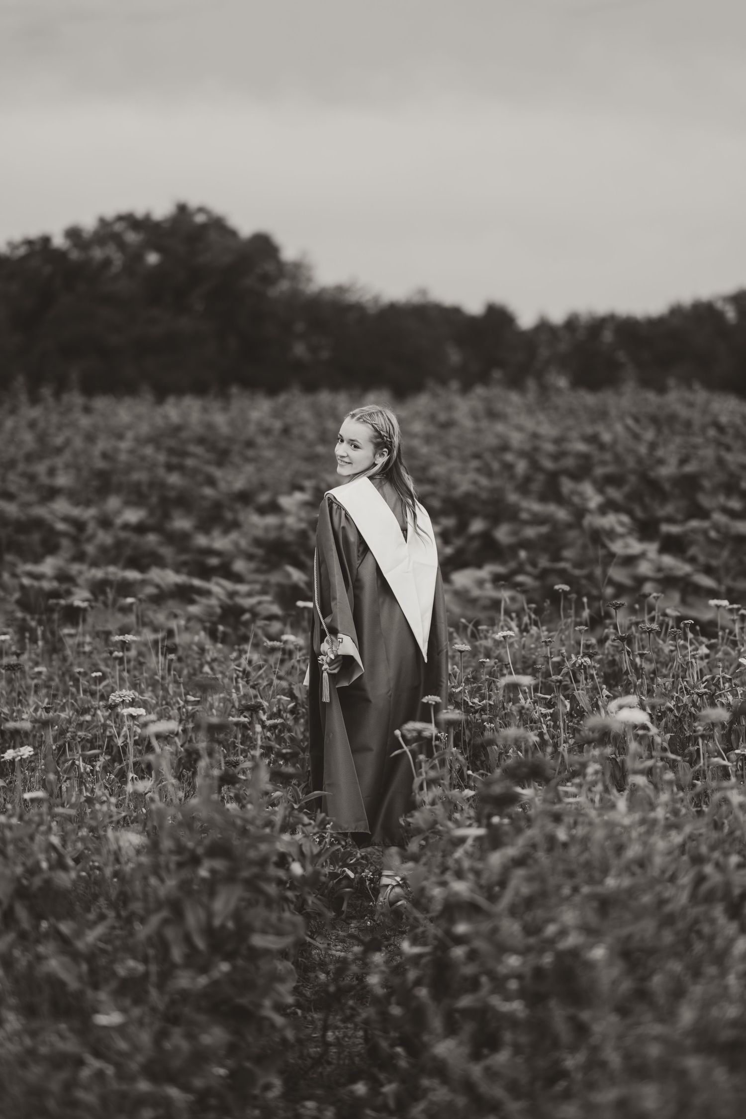 A black and white portrait in a flowering meadow wearing academic regalia.