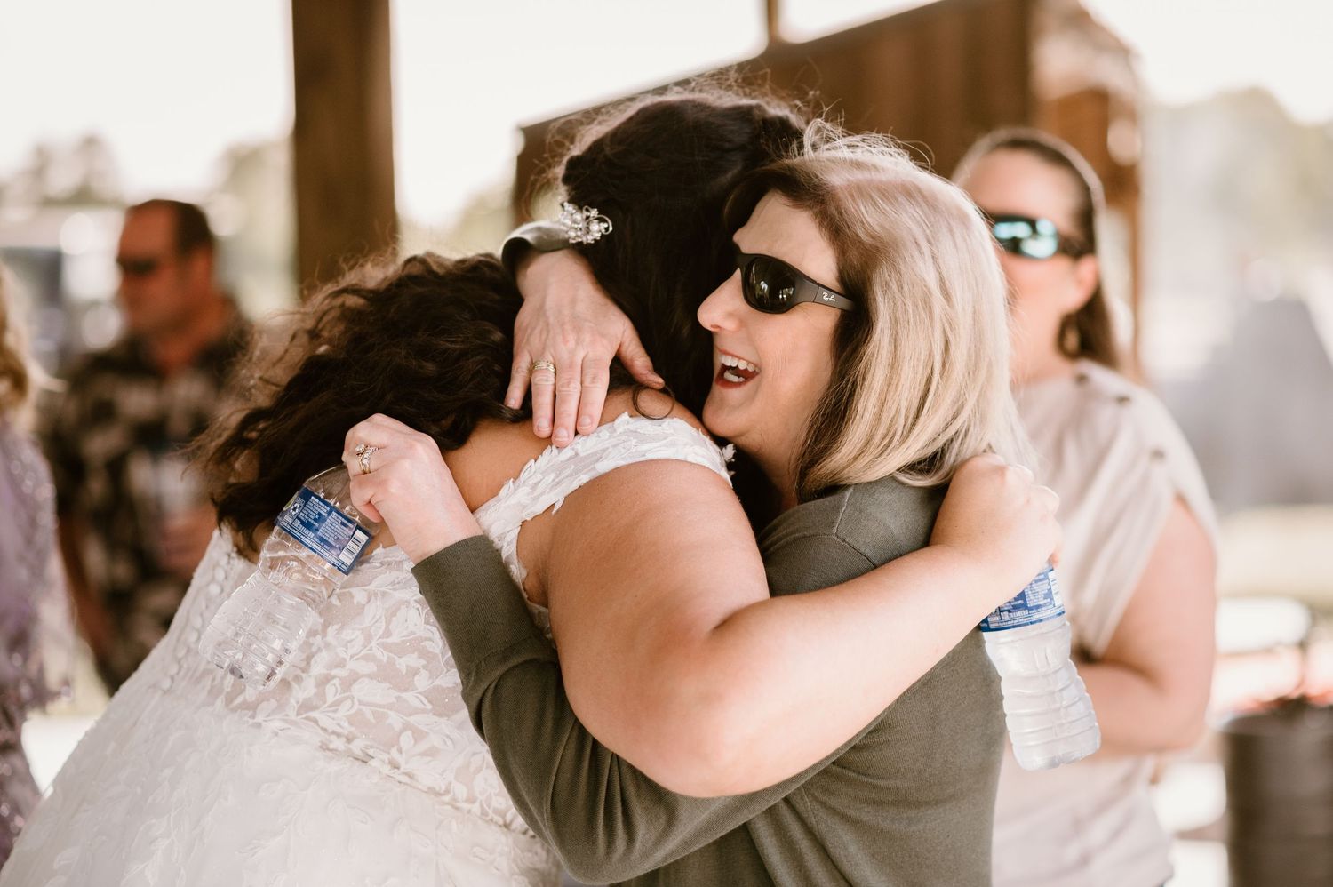 Emotional embrace between wedding guests during outdoor reception celebration.