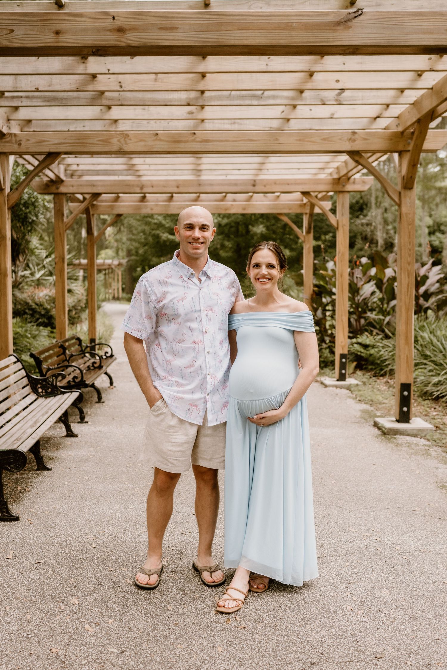 Couple in light blue dress and white shirt posing under wooden pergola.