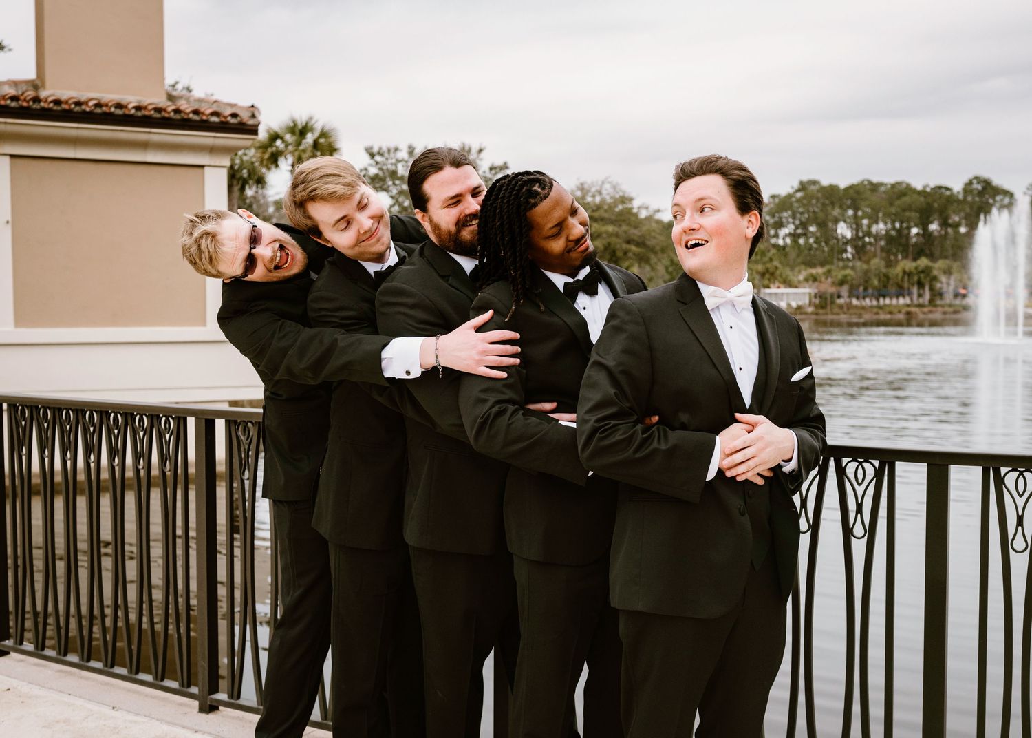 Groomsmen in black tuxedos huddled together in a candid moment.
