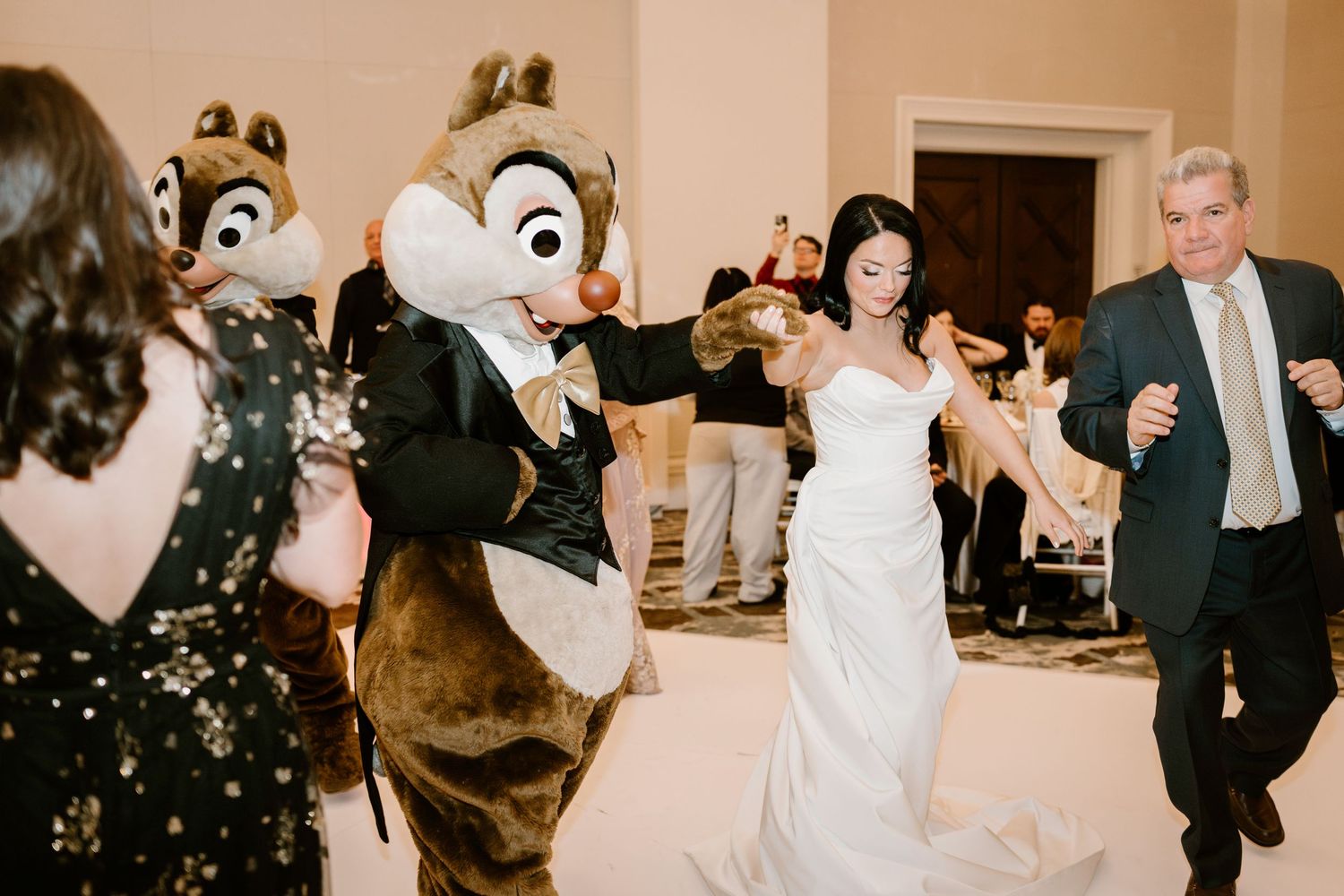 Disney chipmunk mascots dance with wedding guests during a reception celebration.