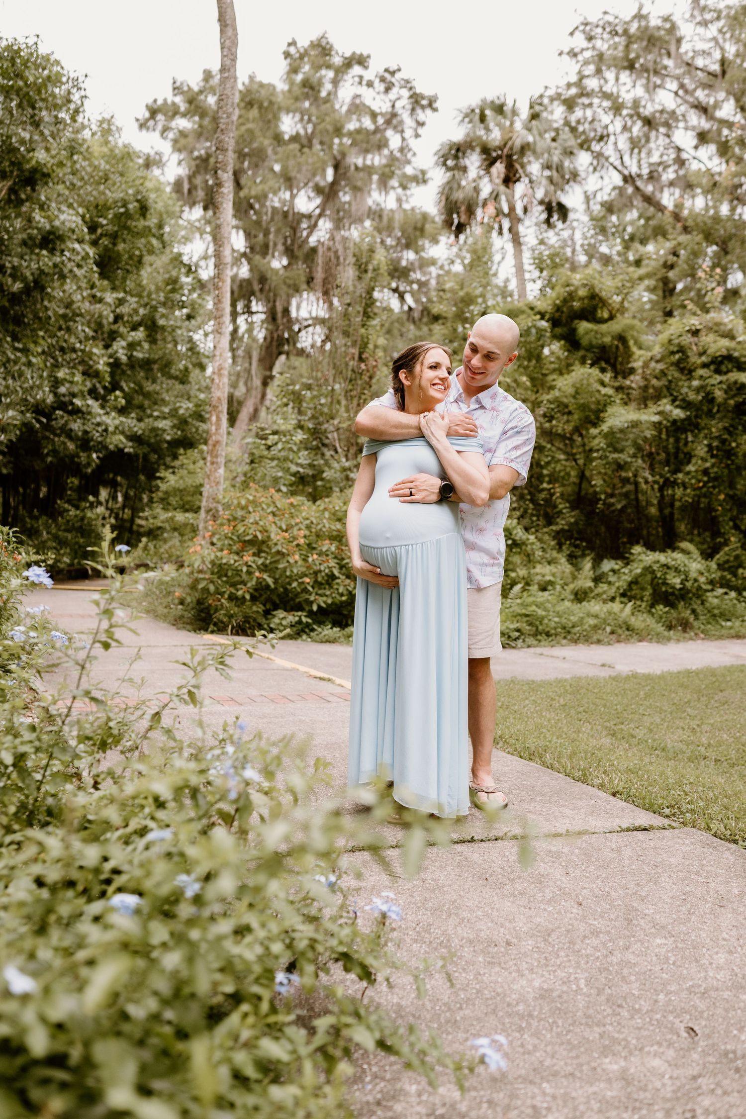 Romantic outdoor photoshoot with couple in light blue dress and white shirt on garden path.
