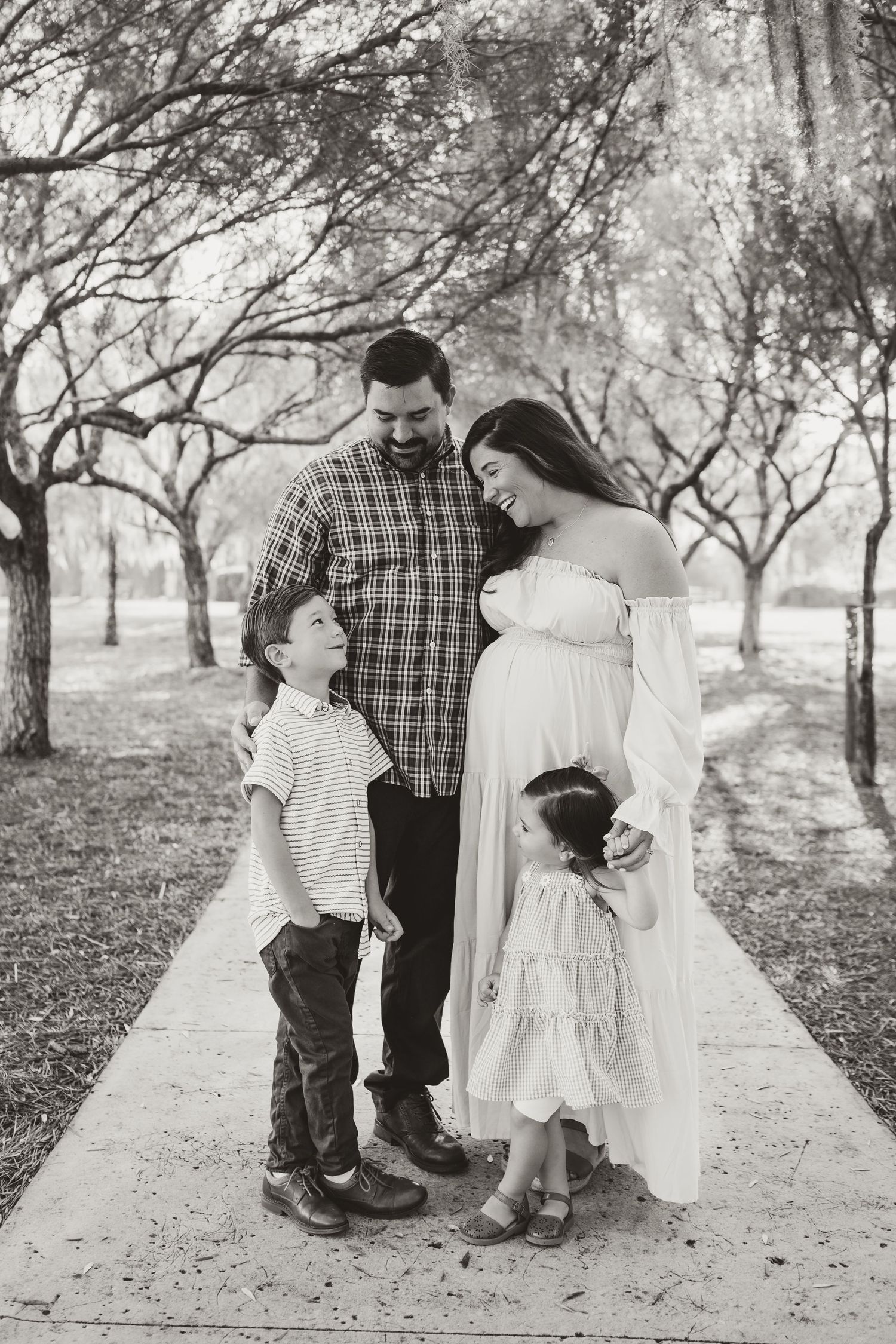 A family of four poses together on a tree-lined path in black and white.