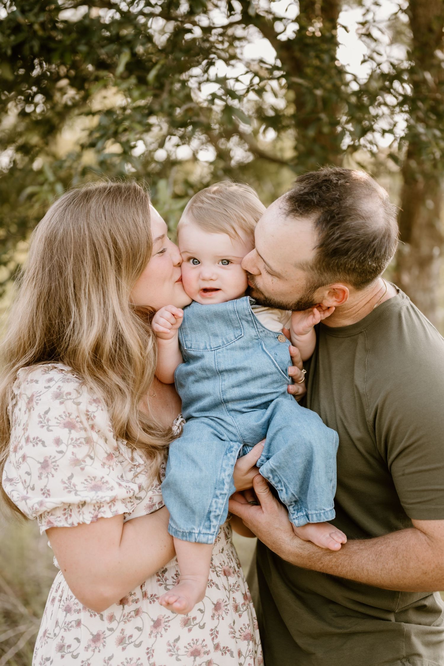 Family sharing tender moment with baby in denim outfit during outdoor photoshoot.
