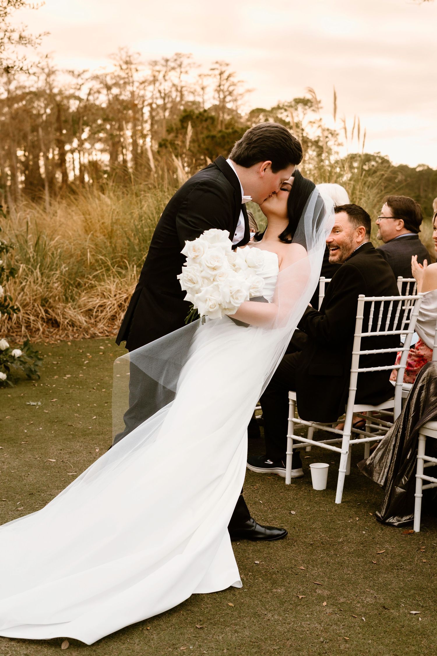 A dramatic wedding pose captured during an outdoor ceremony with white chairs in the background.