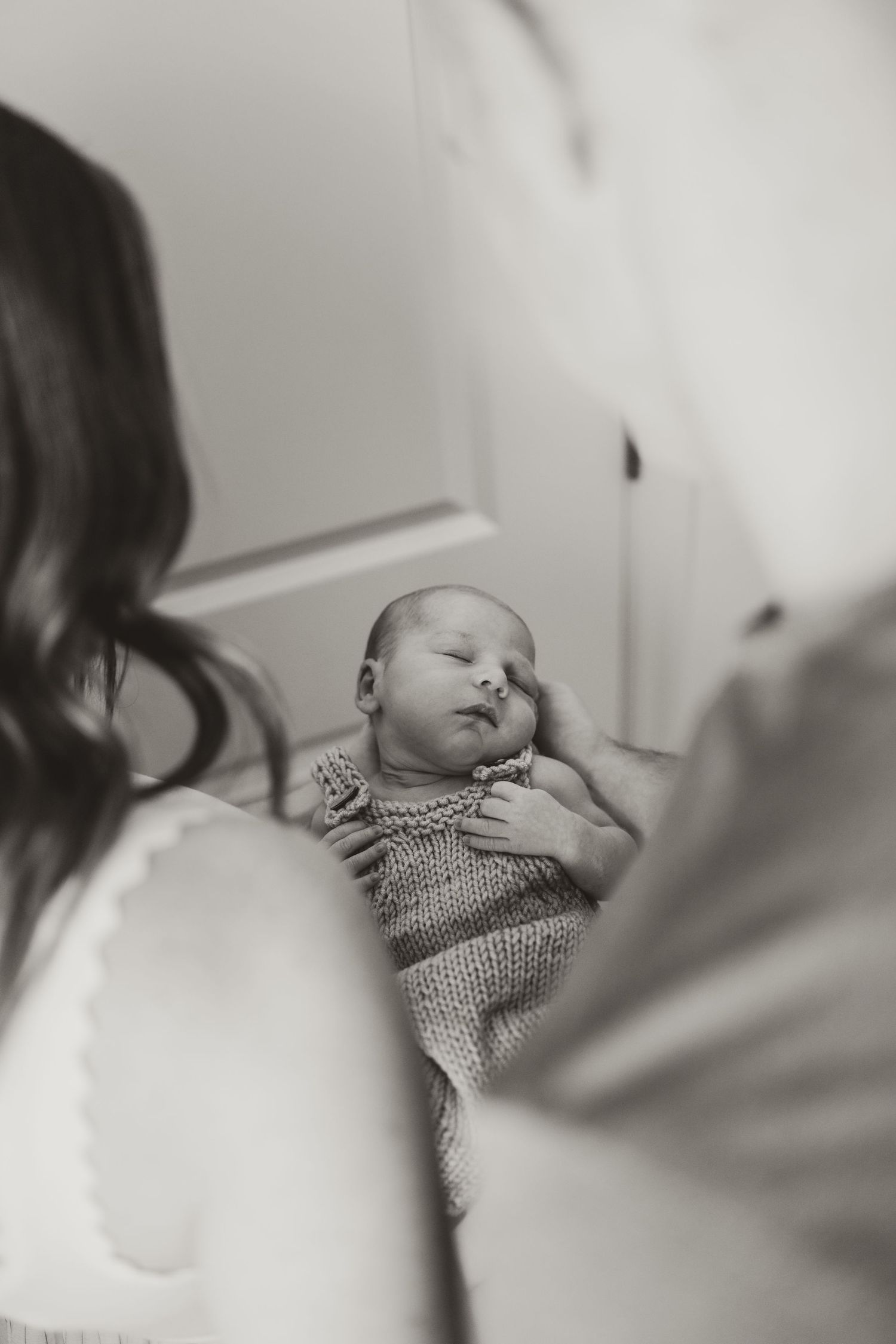 Black and white image of a peaceful sleeping baby in knitted clothing.