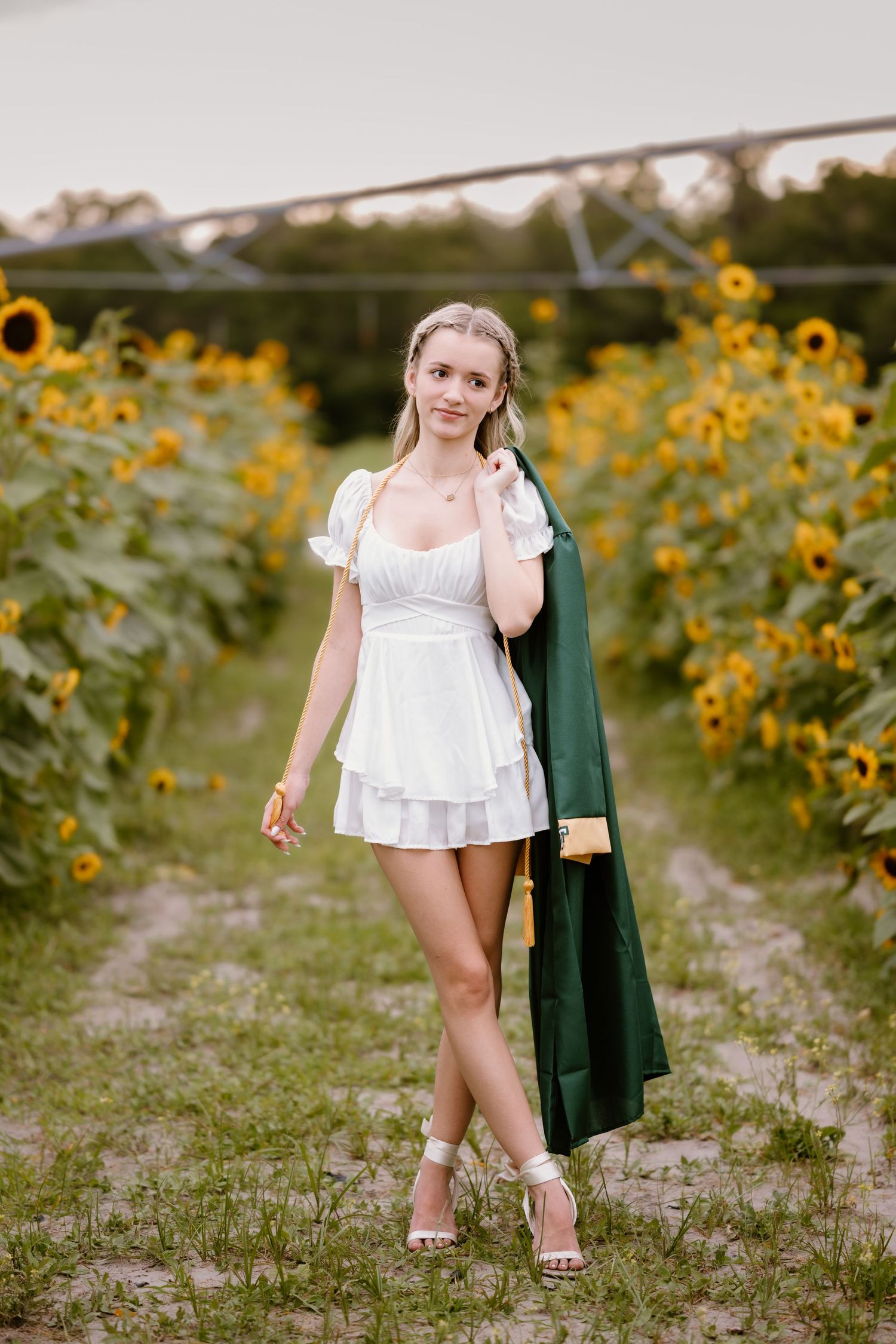 Person in white dress walks through sunflower field carrying a green jacket.
