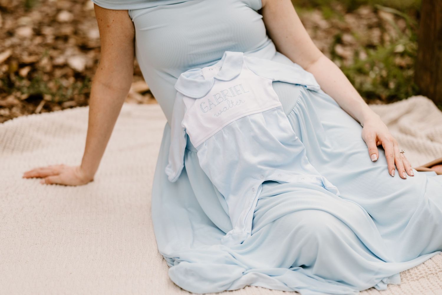 Woman in light blue dress sitting on sandy ground during outdoor photoshoot.